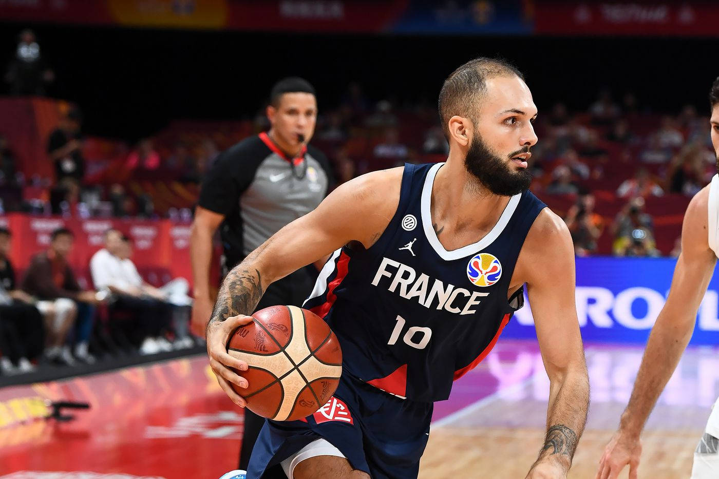 伊萬·福尼爾 法國對阿根廷 2019 FIBA世界盃 壁紙 — 一位身穿海軍藍球衣的法國籃球運動員在明亮的場館燈光下，於一場激烈的比賽中奮力運球。
