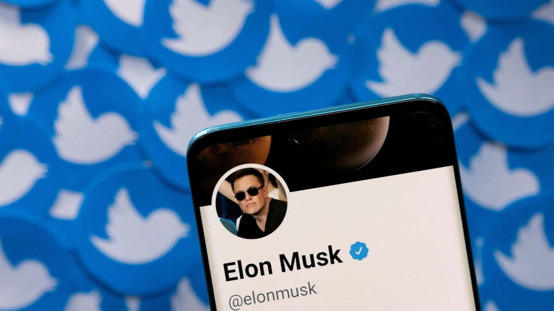 手機特寫，顯示Elon Musk的Twitter個人資料，背景為藍色鳥標誌。 — 馬斯克 壁紙