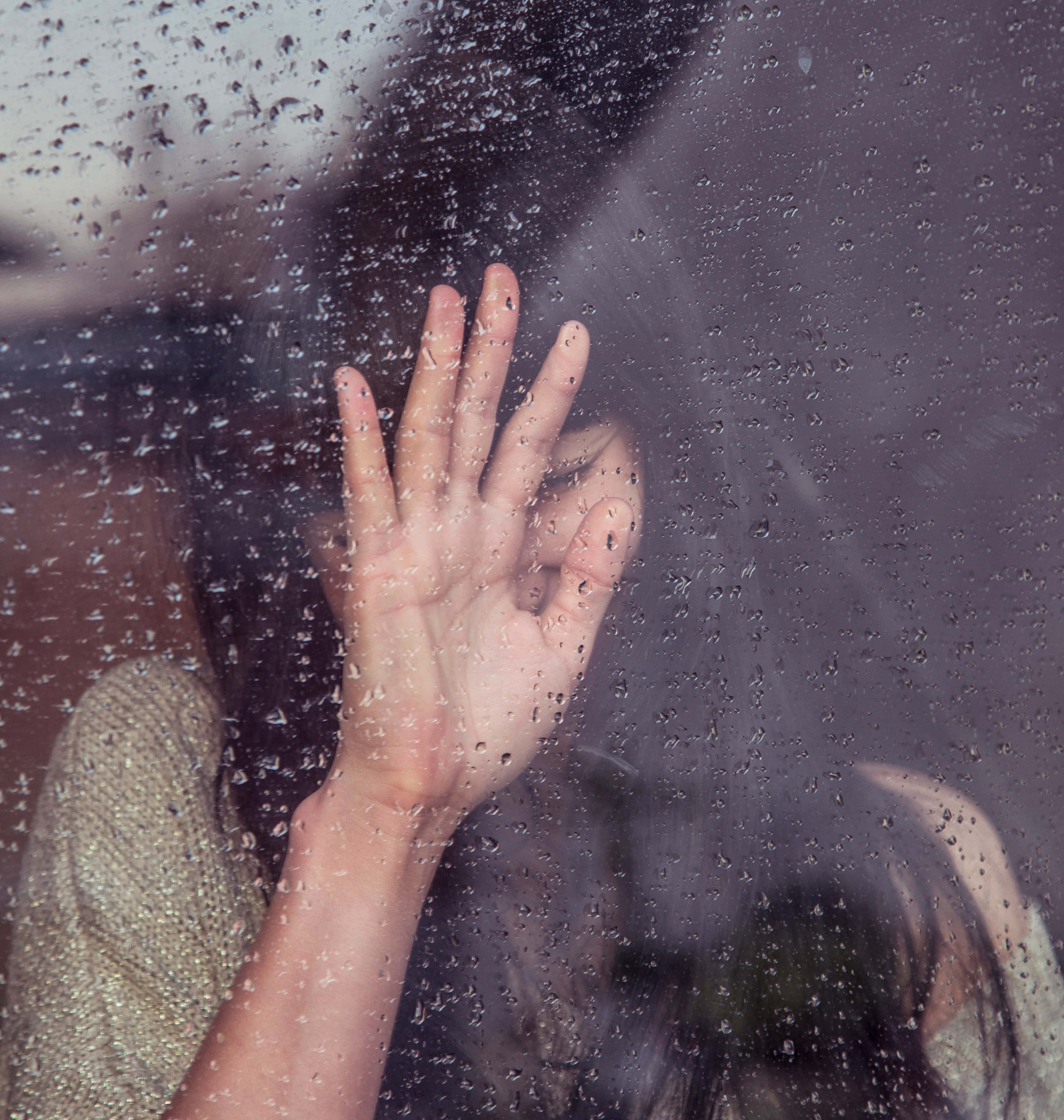 「休息一下沒關係」 壁紙 — 一隻手按在佈滿雨點的窗戶上，玻璃後面可見模糊的深色頭髮和帶有紋理的袖子。