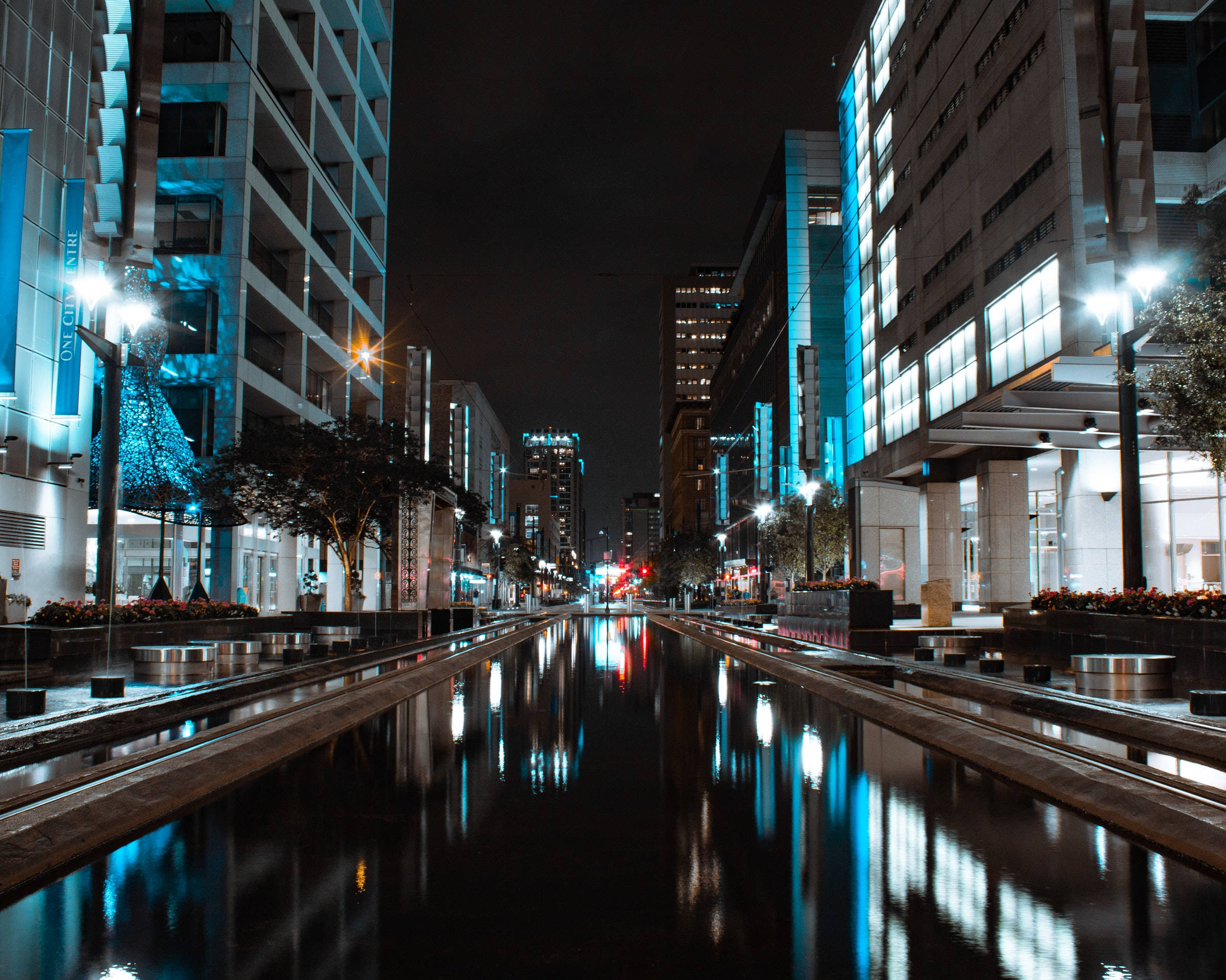 休斯頓主街廣場 壁紙 — 夜晚濕潤的城市運河反射出高聳建築物和街燈發出的藍色和白色光芒。