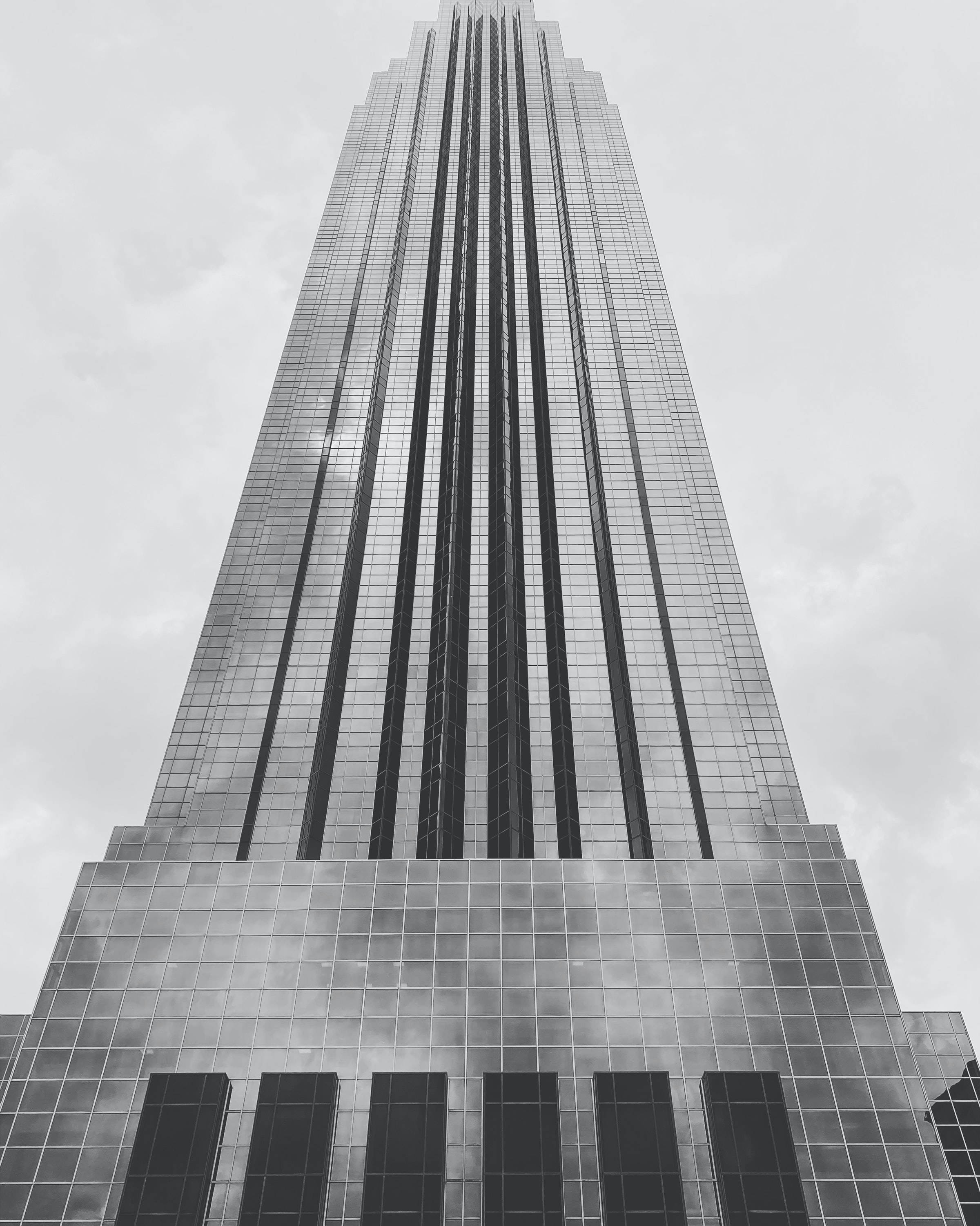 休斯頓威廉姆斯大廈灰階風景 壁紙 — 一座高聳的玻璃摩天大樓在陰雲密佈的天空下以黑白構圖銳利地矗立。