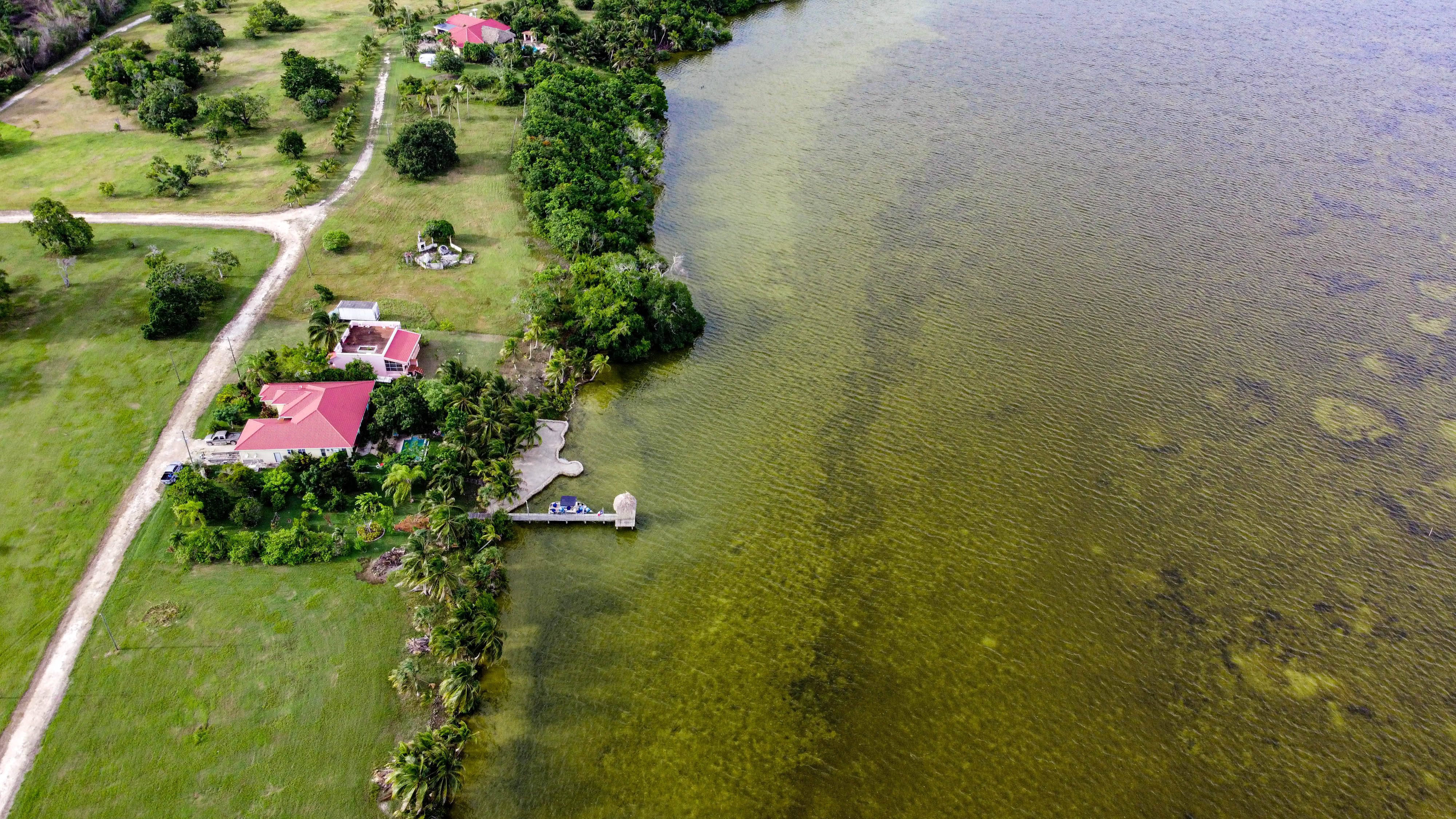 伯利茲普羅格雷索高地 壁紙 — 熱帶海濱物業的鳥瞰圖，紅色屋頂的房子停泊在清澈的綠色水域中，周圍環繞著茂密的綠植。
