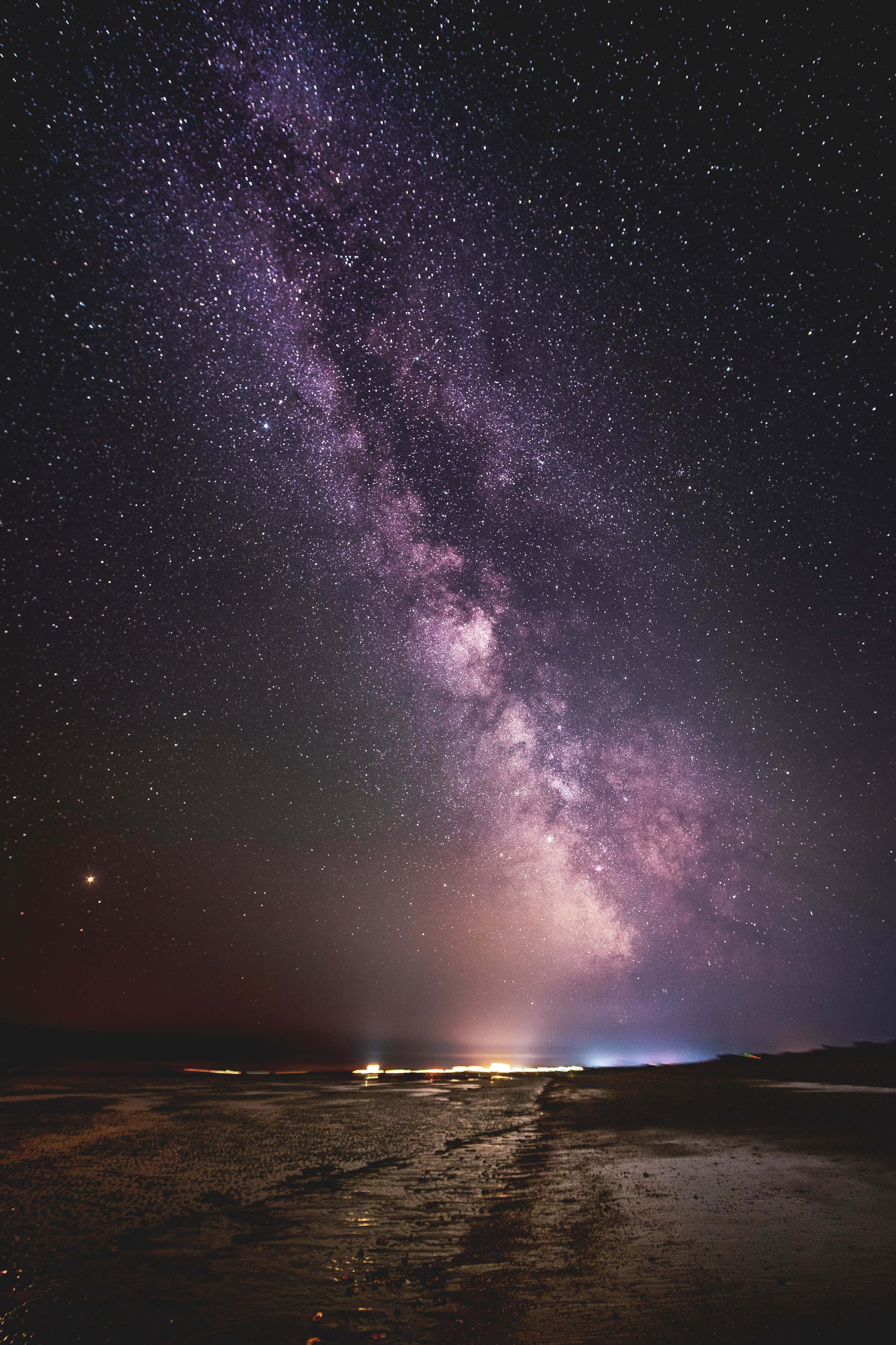 伯利茲遠離塵囂的海灘日落 壁紙 — 夜晚，在黑暗潮濕的海灘上，銀河系散發出鮮豔的紫色和粉紅色光芒，令人嘆為觀止。