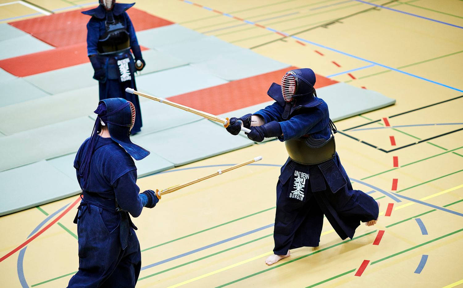 伯恩大學日本武術劍道 壁紙 — 兩名身穿全套裝備的劍道選手在色彩繽紛的體育館地板上交劍。