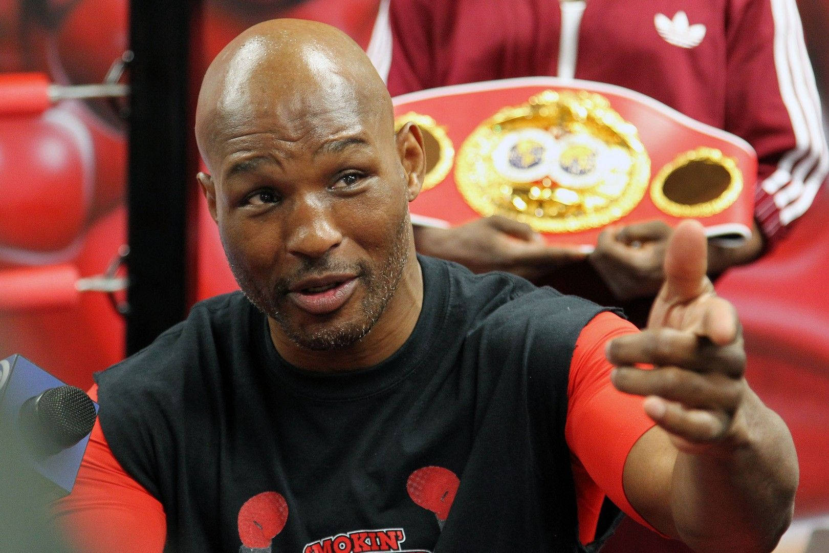 伯納德·霍普金斯與人對話 壁紙 — 拳擊手弗洛伊德·梅威瑟（Floyd Mayweather Jr）在紅黑背景下手持冠軍腰帶，充滿力量地向前指。