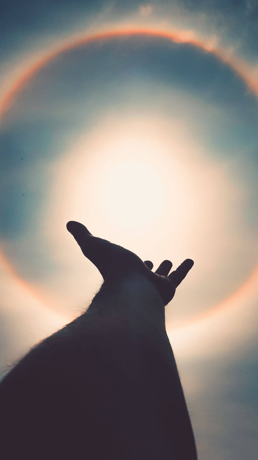 手的剪影伸向天空中有彩色光暈的太陽。