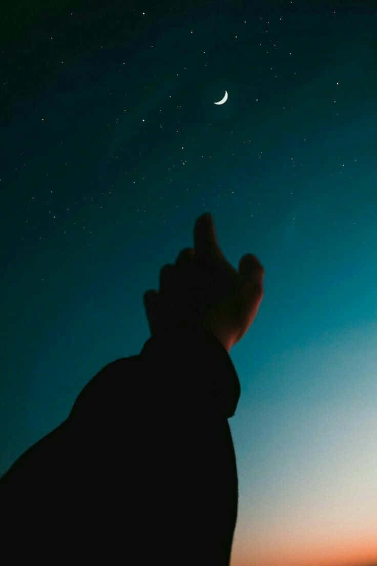 剪影手指向新月和星星，暮色天空。