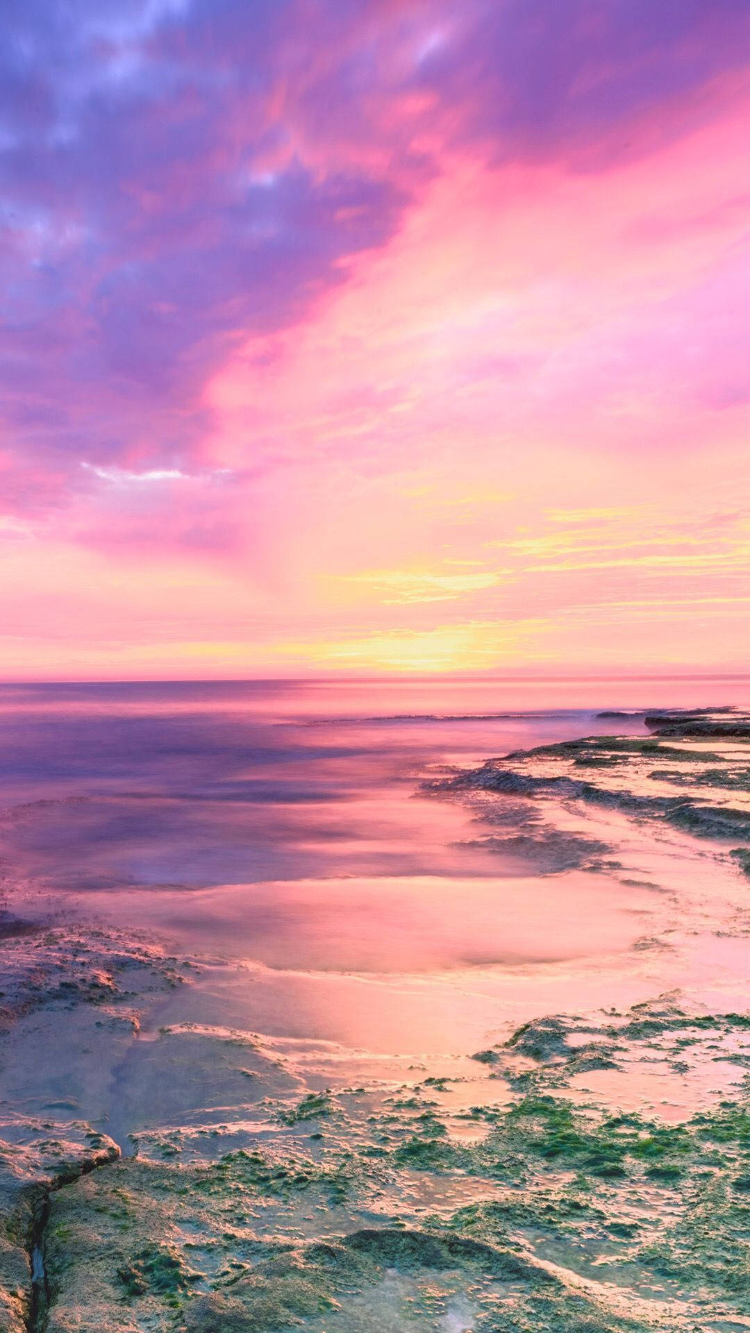 平靜海洋與質感海岸線上的粉紅和紫色夕陽