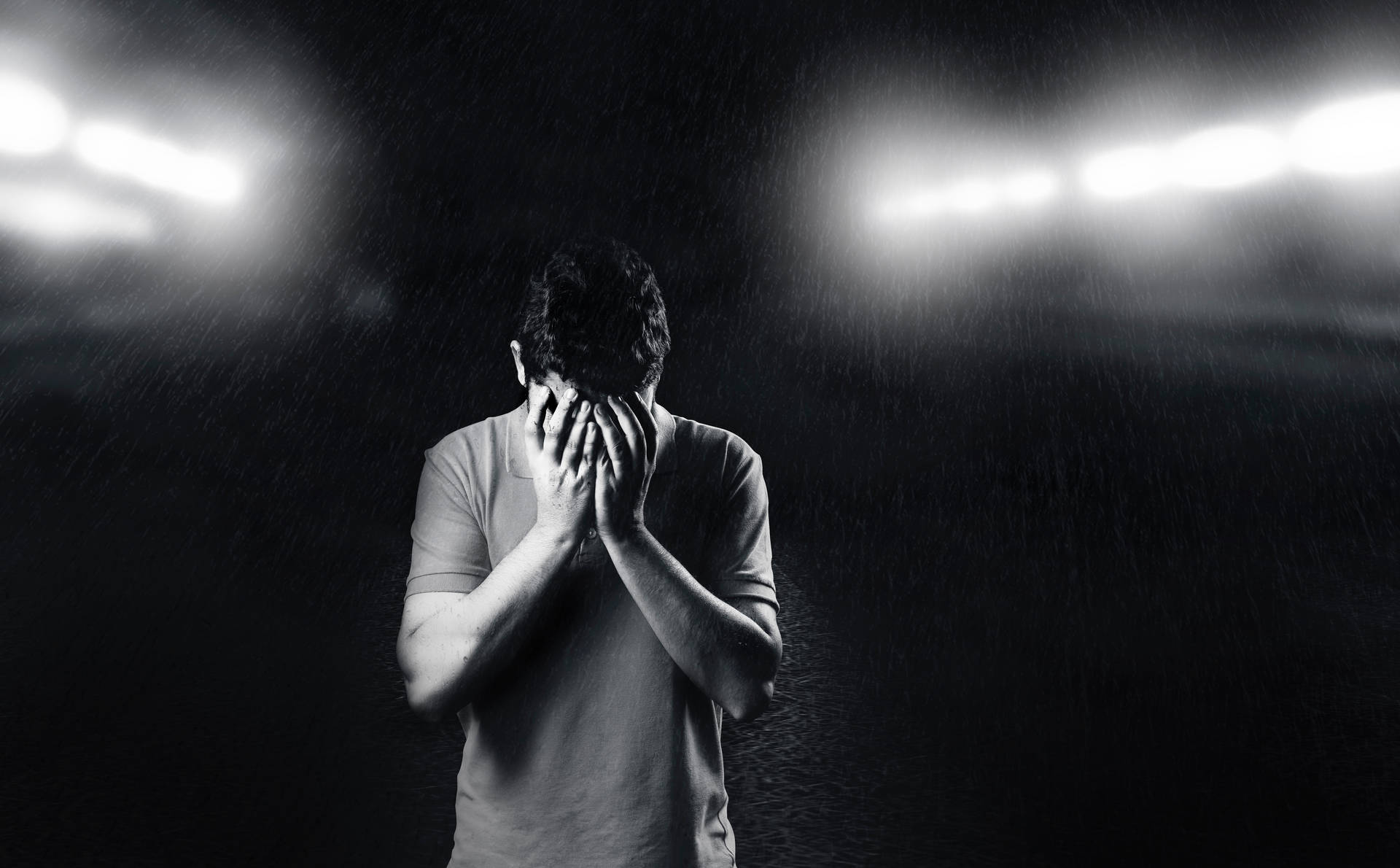 男子在雨中於球場燈光下掩面