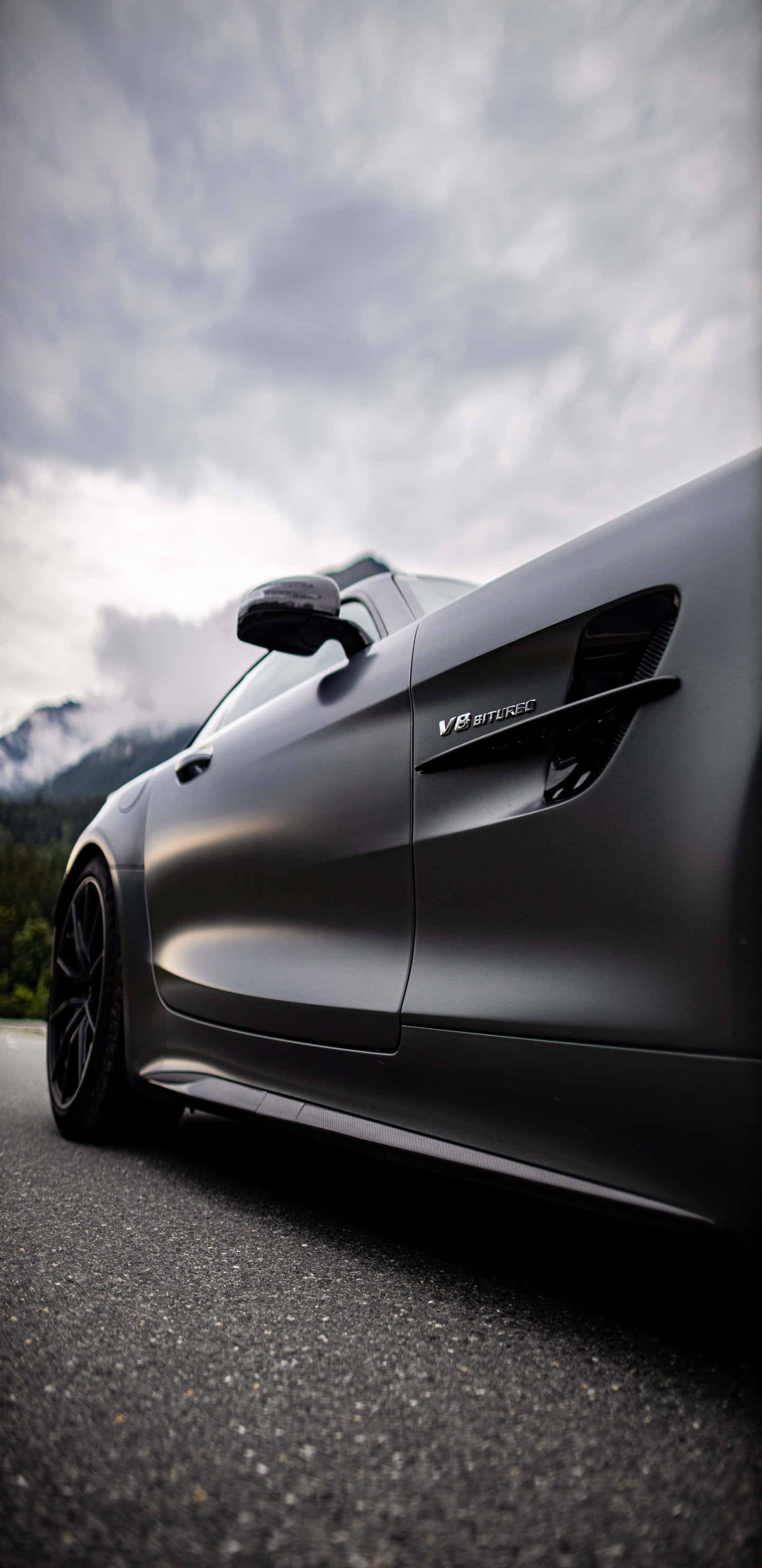 低角度側面黑色梅賽德斯-奔馳 AMG GT-R 背景 壁紙 — 一架時尚的啞光黑色跑車停在瀝青路上，背景是霧氣繚繞的山巒和陰天。