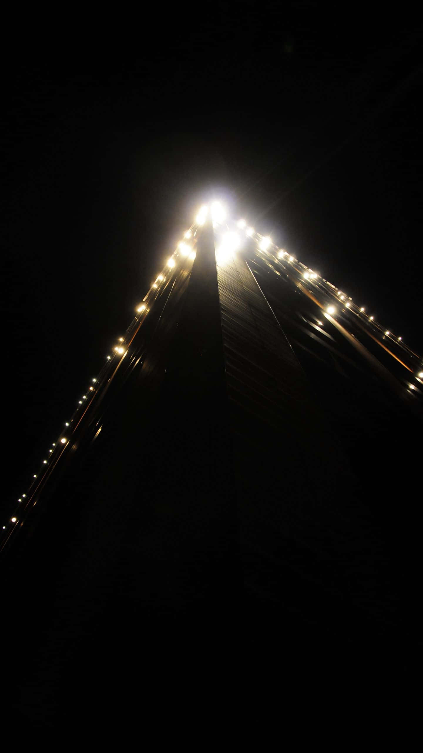 Dark Corner 桌布 壁紙 — 低角度夜攝，一座燈火通明的橋樑伸入黑暗，邊緣有發光的街燈。