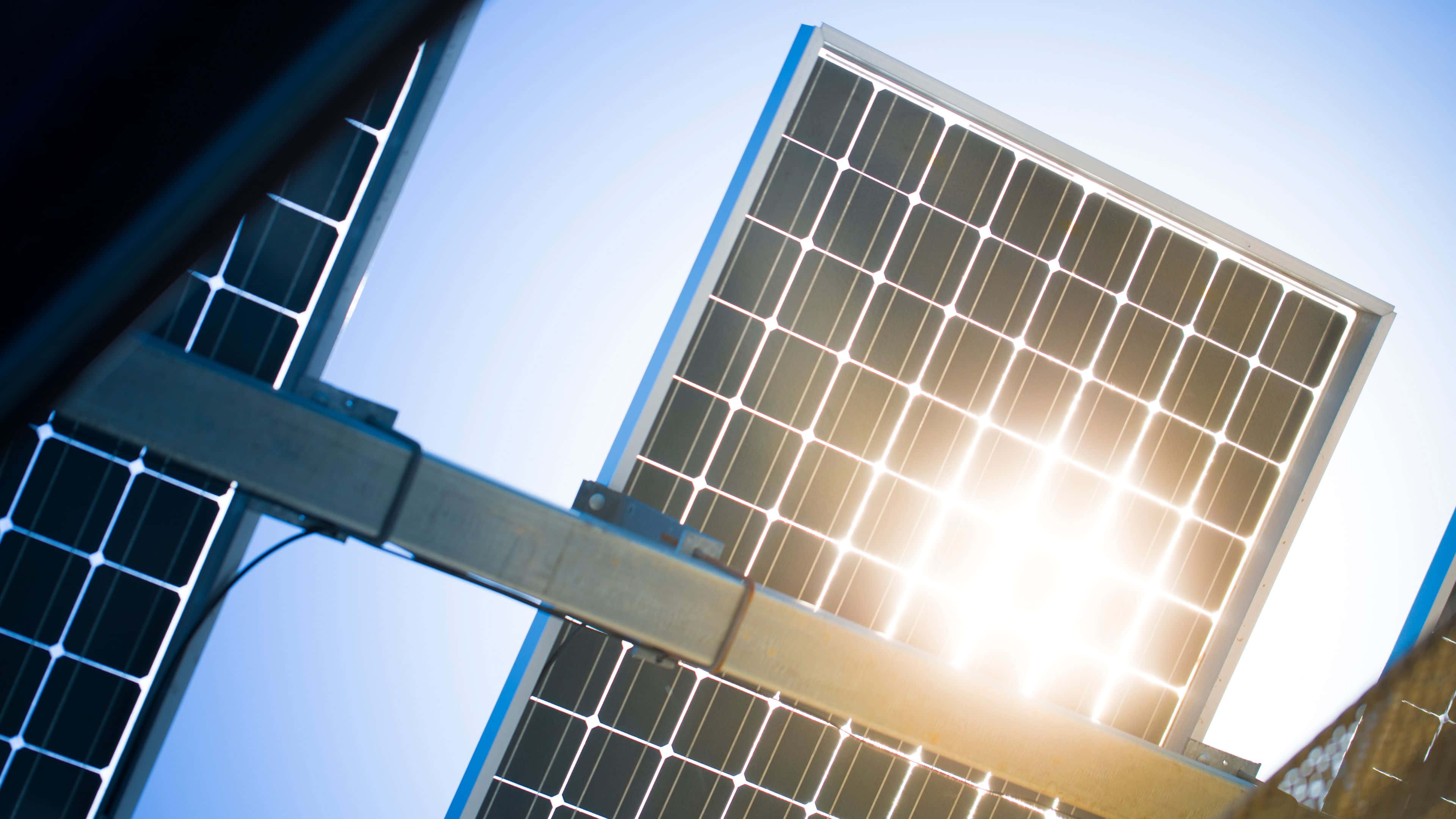 Solar Panel 桌布 壁紙 — 低角度拍攝太陽能板在晴朗藍天下捕捉明亮陽光的照片。