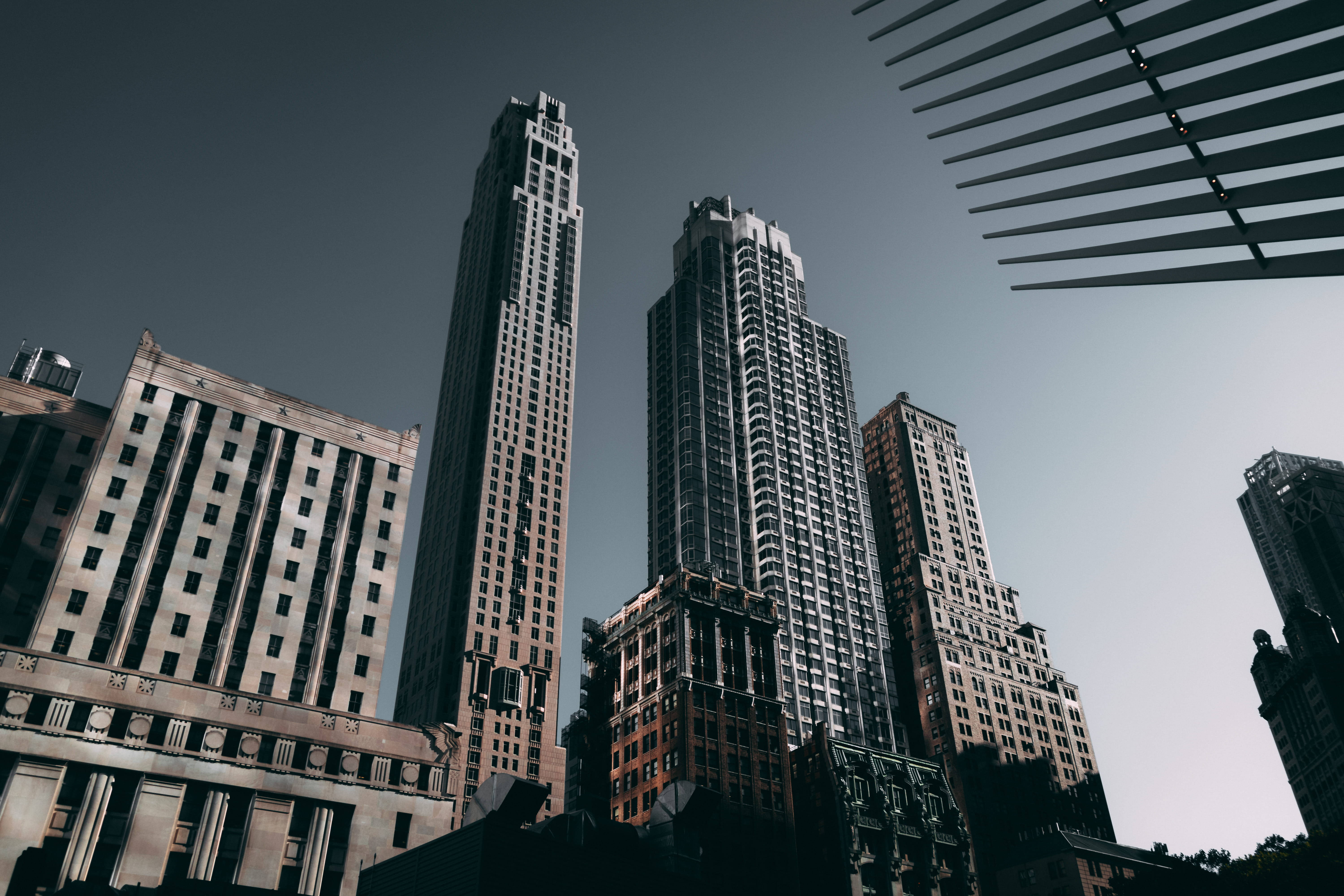 New York 桌布 壁紙 — 低角度拍攝密集城市峽谷中高聳的摩天大樓，天空柔和，建築細節突出。