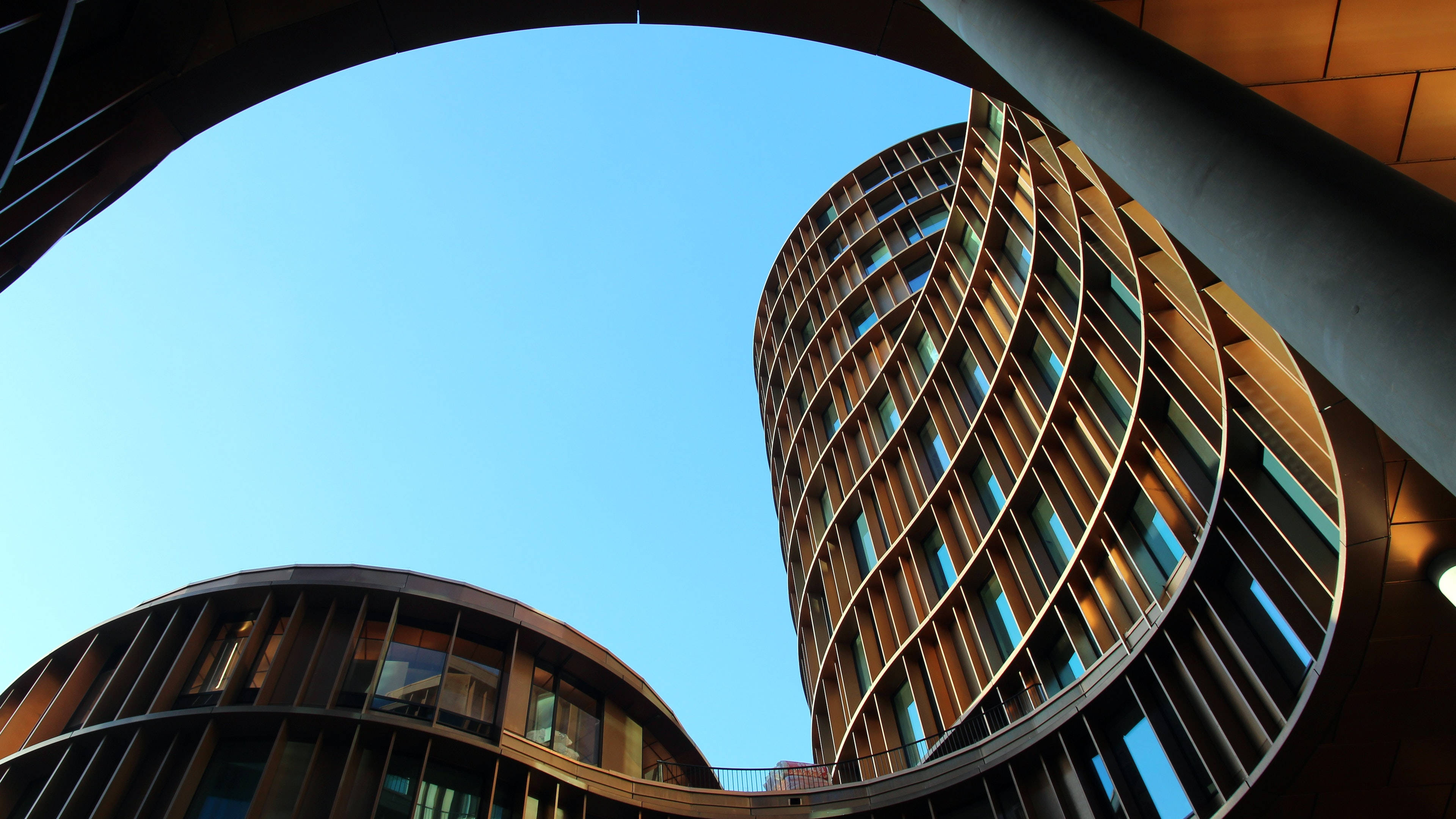 Buildings 桌布 壁紙 — 低角度拍攝捕捉到兩座彎曲的木建築，以現代建築線條框住清澈的藍天。