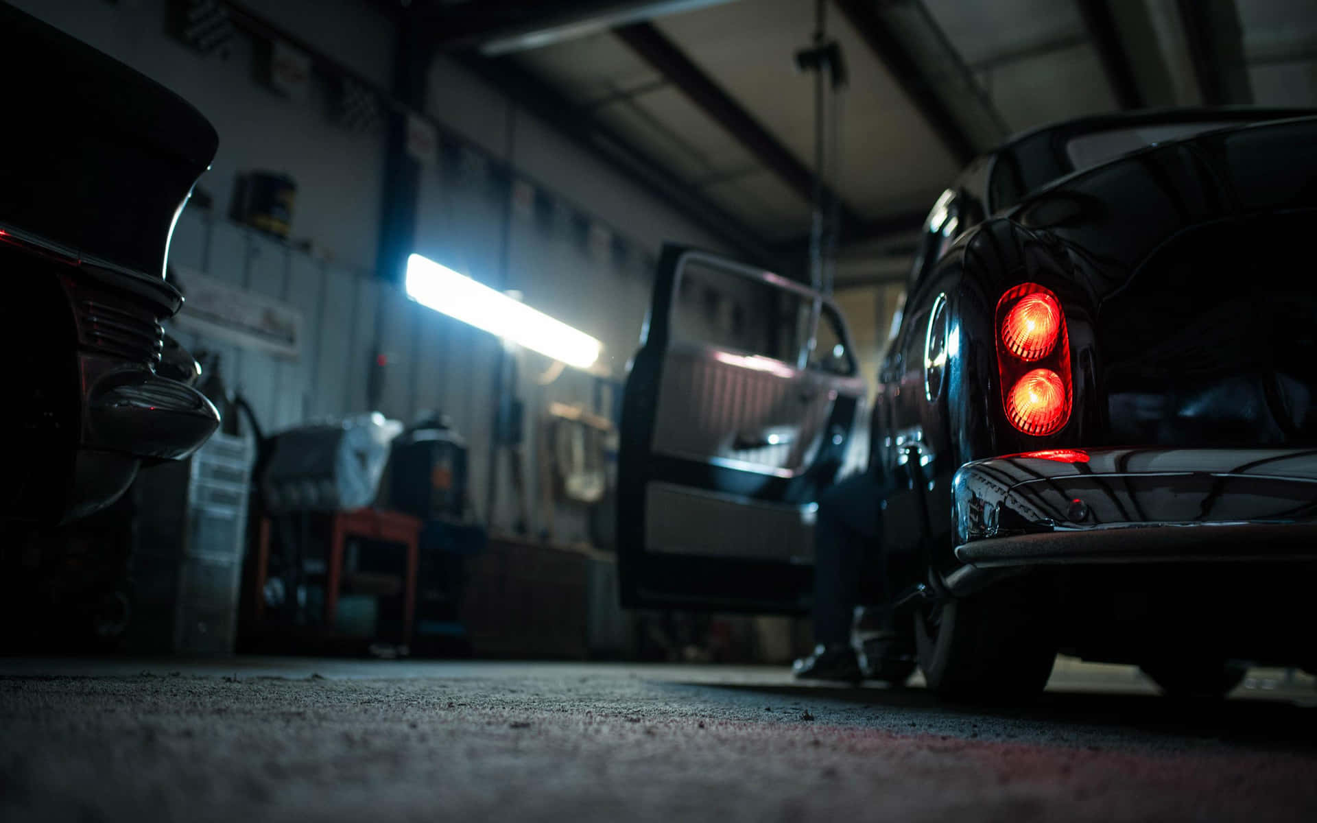 Garage 桌布 壁紙 — 低角度拍攝昏暗車庫中的老爺車，紅色尾燈發光，頭頂有螢光燈。