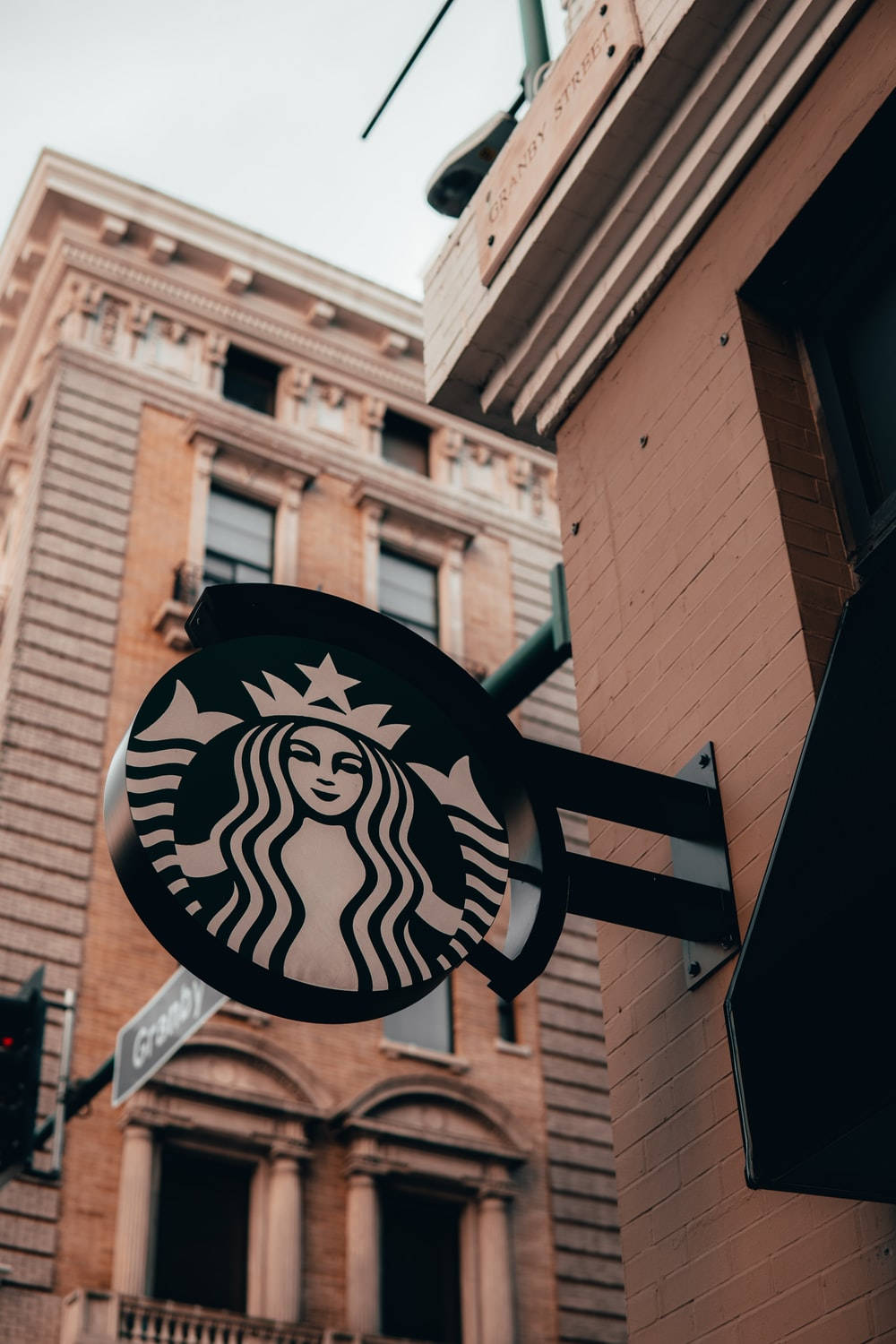 Building 桌布 壁紙 — 低角度拍攝的Starbucks標誌招牌，安裝在磚砌建築上，背景為多雲的天空。