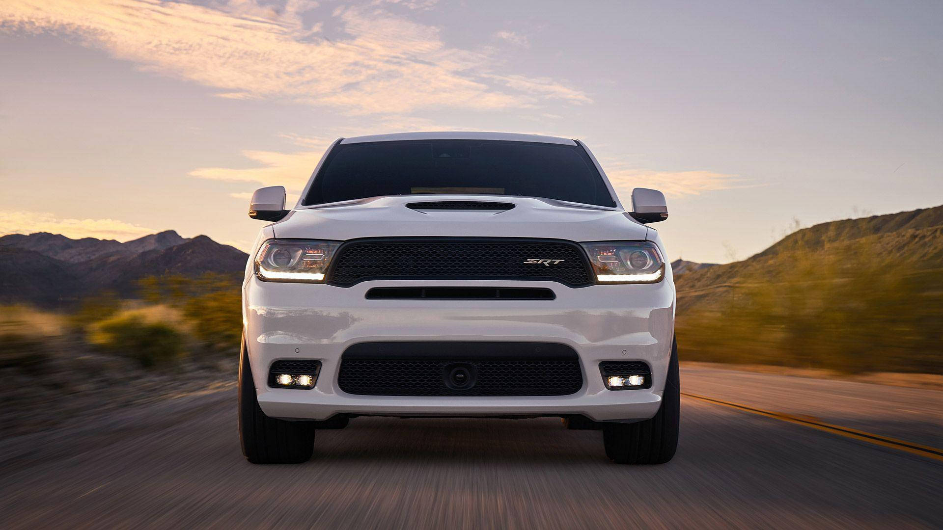 低角度白色杜蘭戈前視 壁紙 — 一輛白色Dodge Ram SRT卡車在日落時分的沙漠公路上向鏡頭疾馳，背景是模糊的山脈。