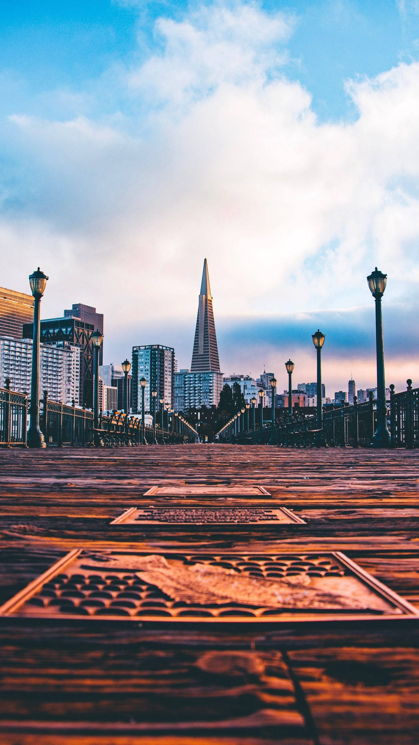 San Francisco Phone 桌布 壁紙 — 低角度觀看一條木製碼頭，在日落時分通往三藩市的天際線，泛美金字塔在柔和的雲層下閃耀。