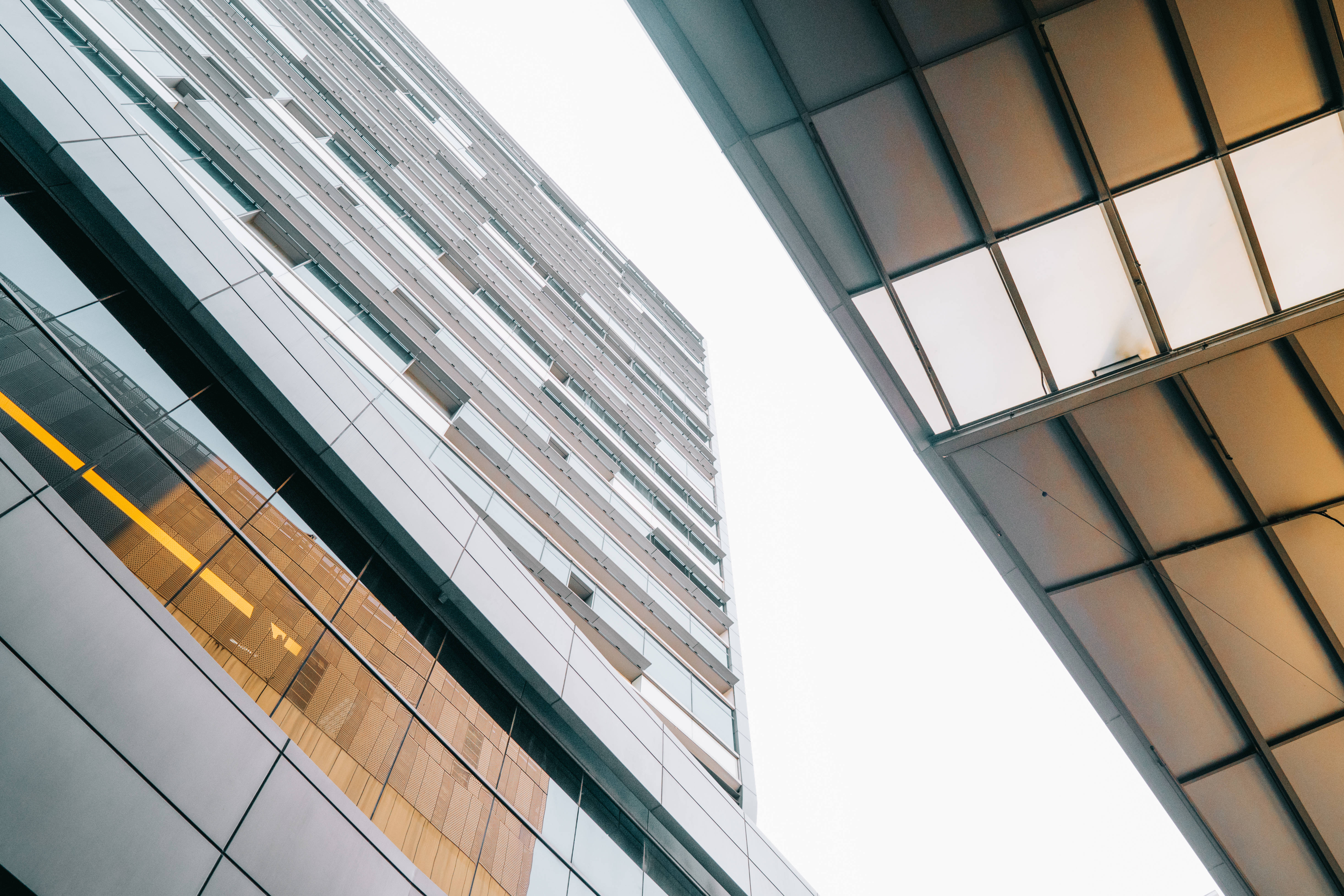 Building 桌布 壁紙 — 低角度觀看現代玻璃和鋼鐵摩天大樓，溫暖的室內燈光映照在明亮的天空上。
