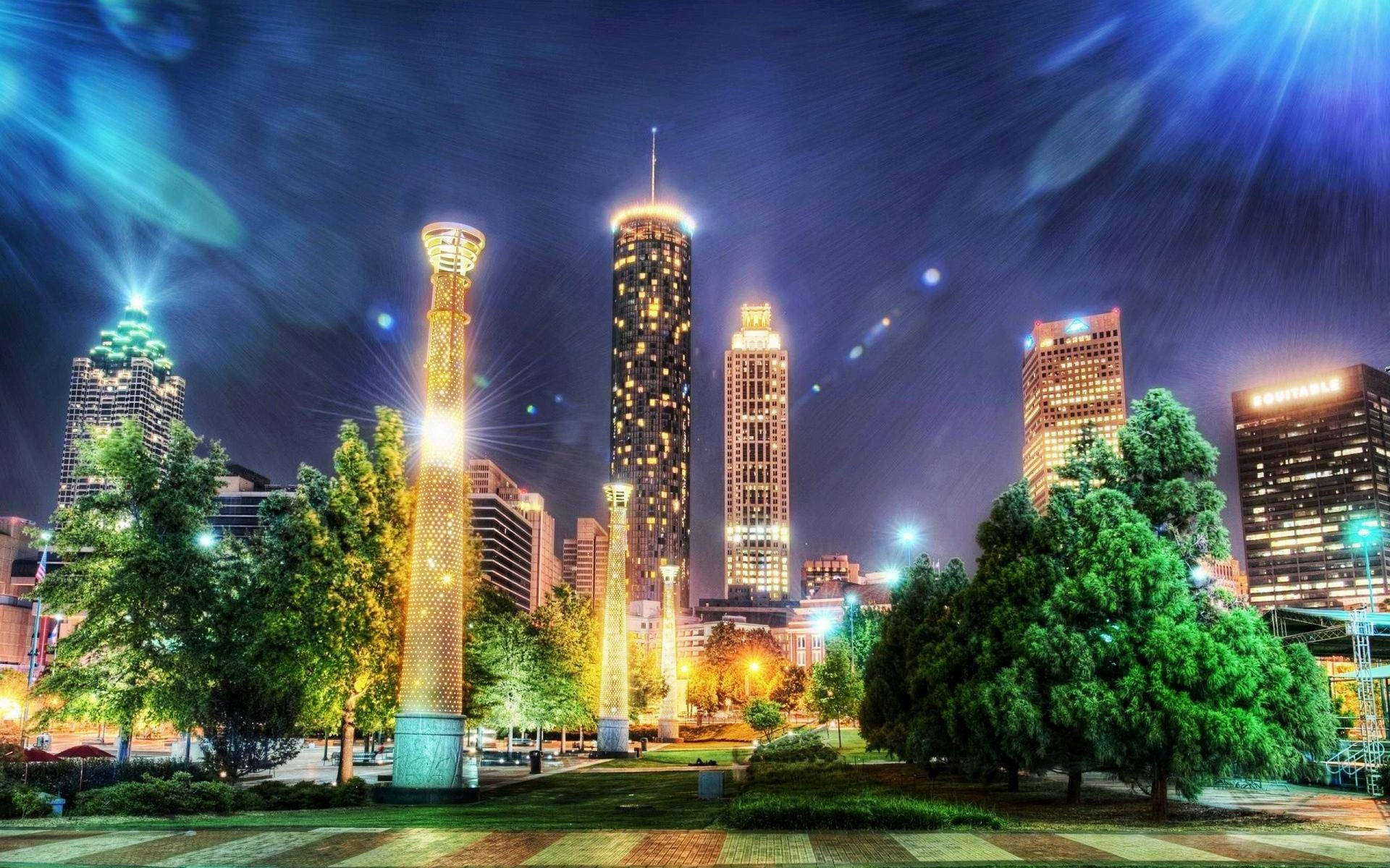 佐治亞州亞特蘭大建築夜景 壁紙 — 充滿活力的夜景，點亮的摩天大樓和發光的塔樓被茂密的綠樹環繞，星空璀璨。
