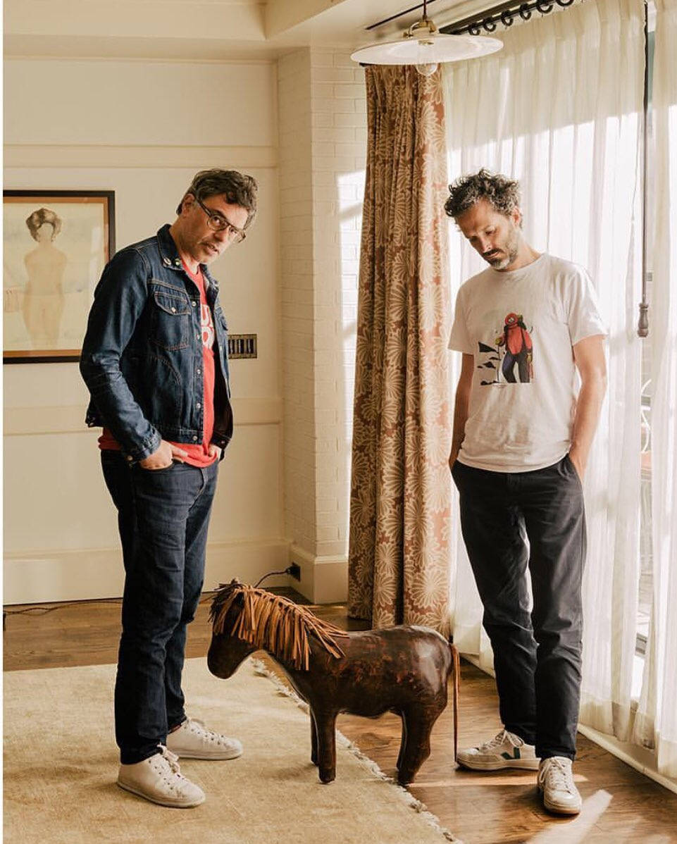 佛萊迪與康奇ords與木馬雕像 壁紙 — 兩個男人企喺一個陽光充足嘅房入面，喺一個有圖案窗簾嘅窗旁邊嘅一個木馬雕像旁邊。