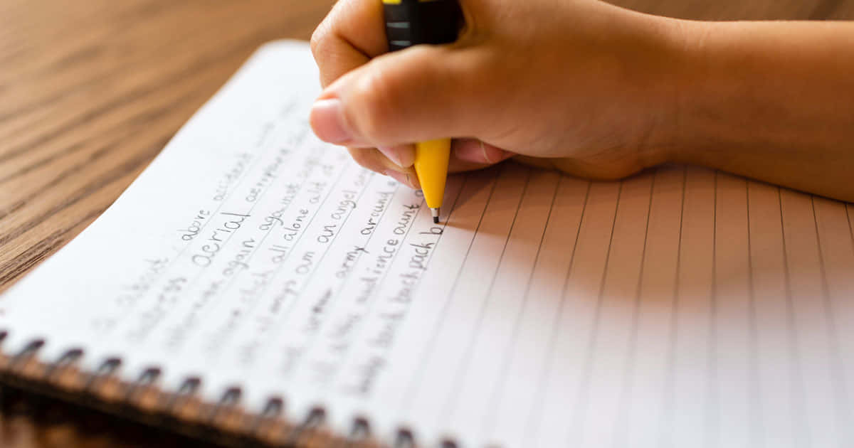 手用黃色筆在螺旋筆記本上書寫草書，置於木上。