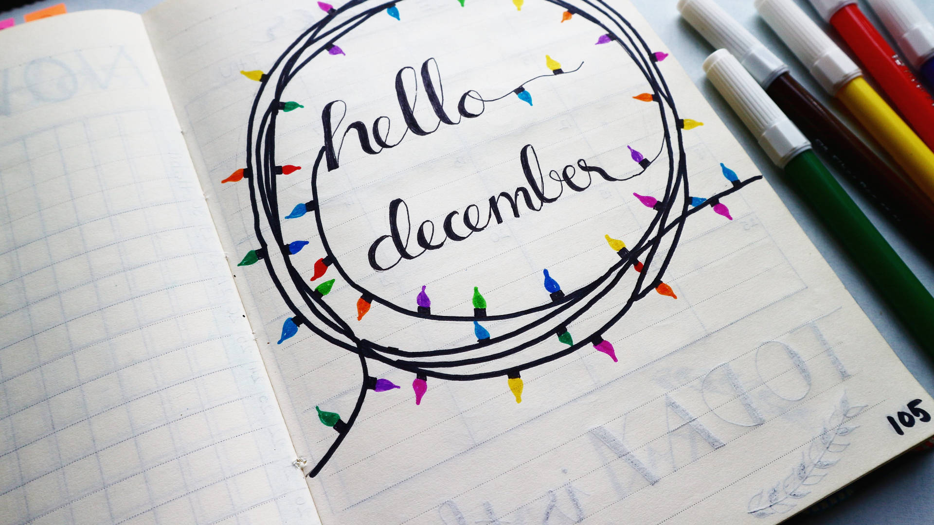 手寫的「hello december」在筆記本中，裝飾著色彩繽紛的燈串，並被記號筆包圍。