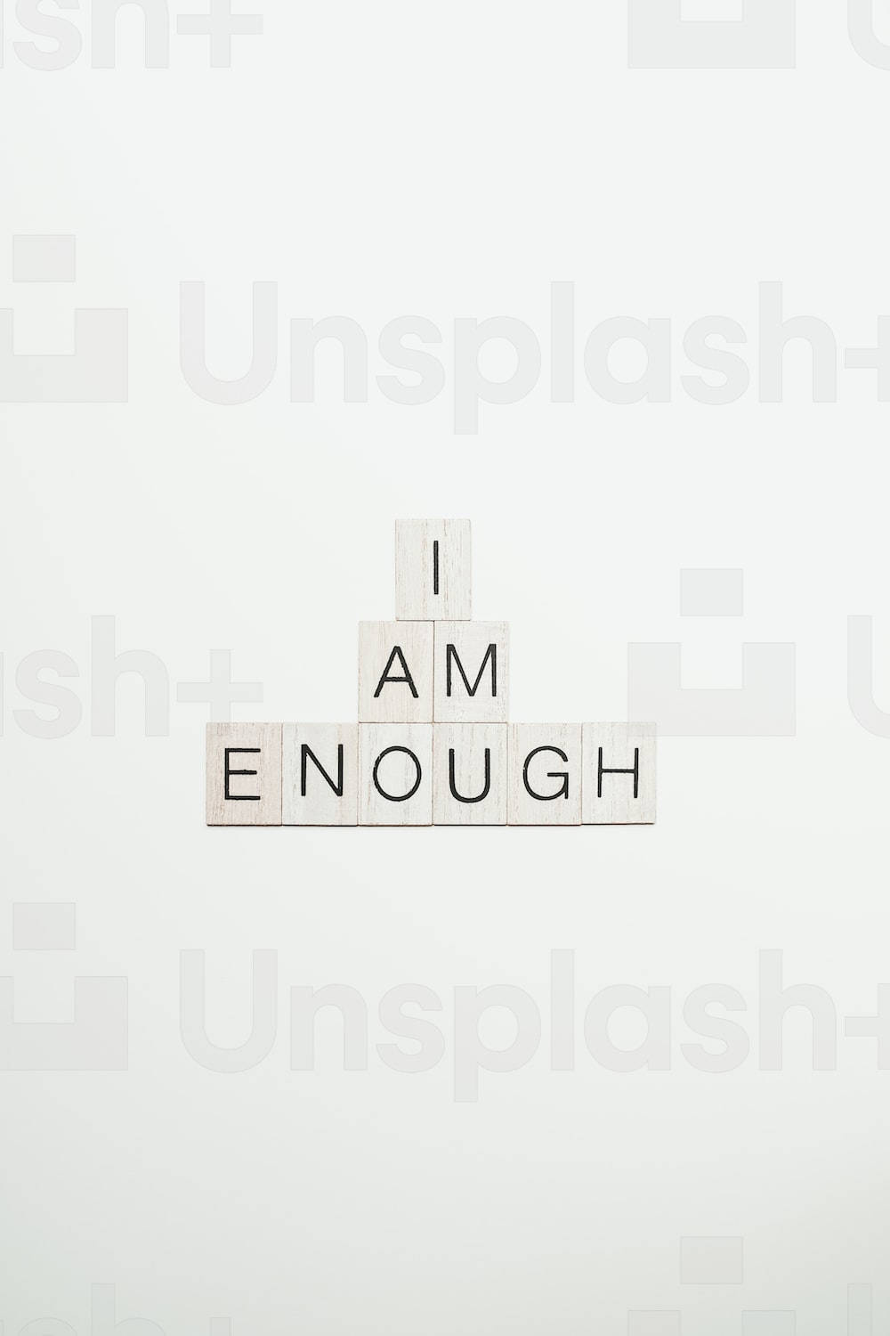 純白背景上以金字塔形狀排列的「I AM ENOUGH」木製拼塊。