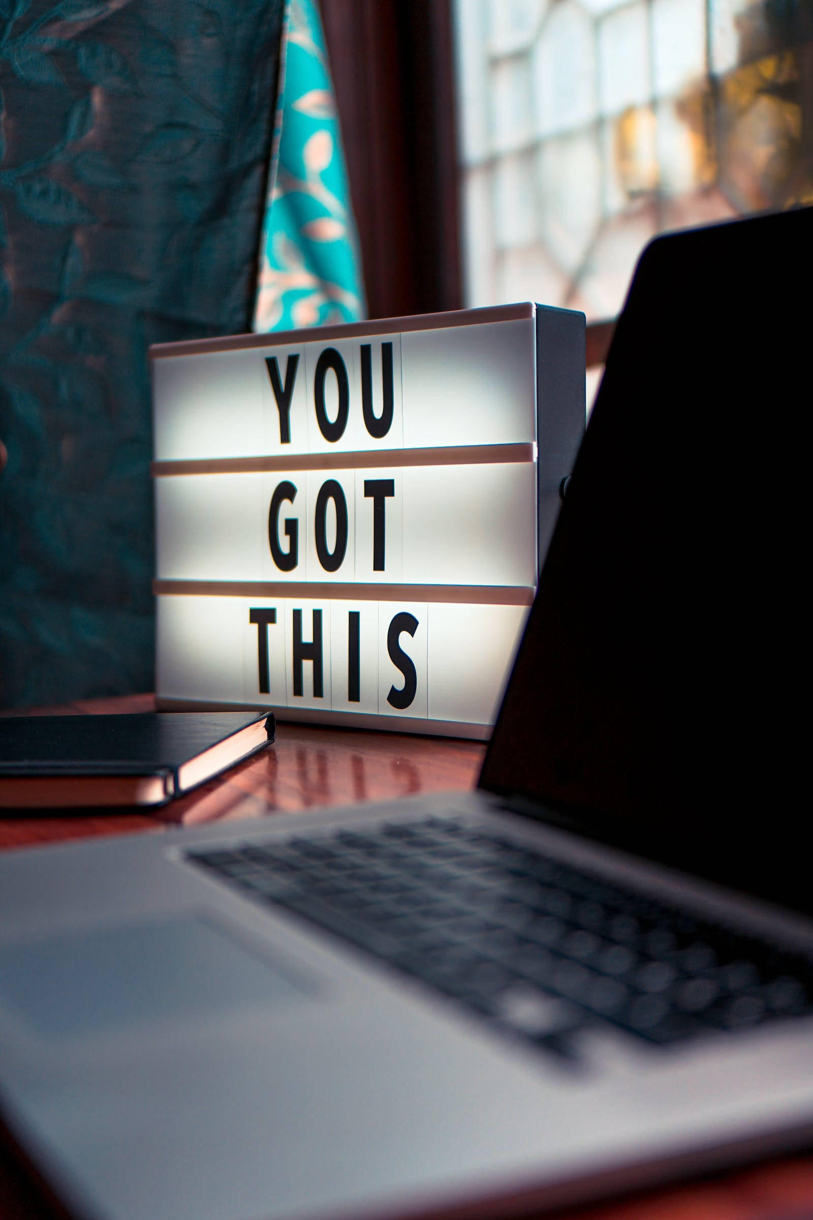 你行的勵志語錄 壁紙 — 一個發光的燈箱，上面寫著「YOU GOT THIS」，放在窗邊木桌的筆記型電腦旁。