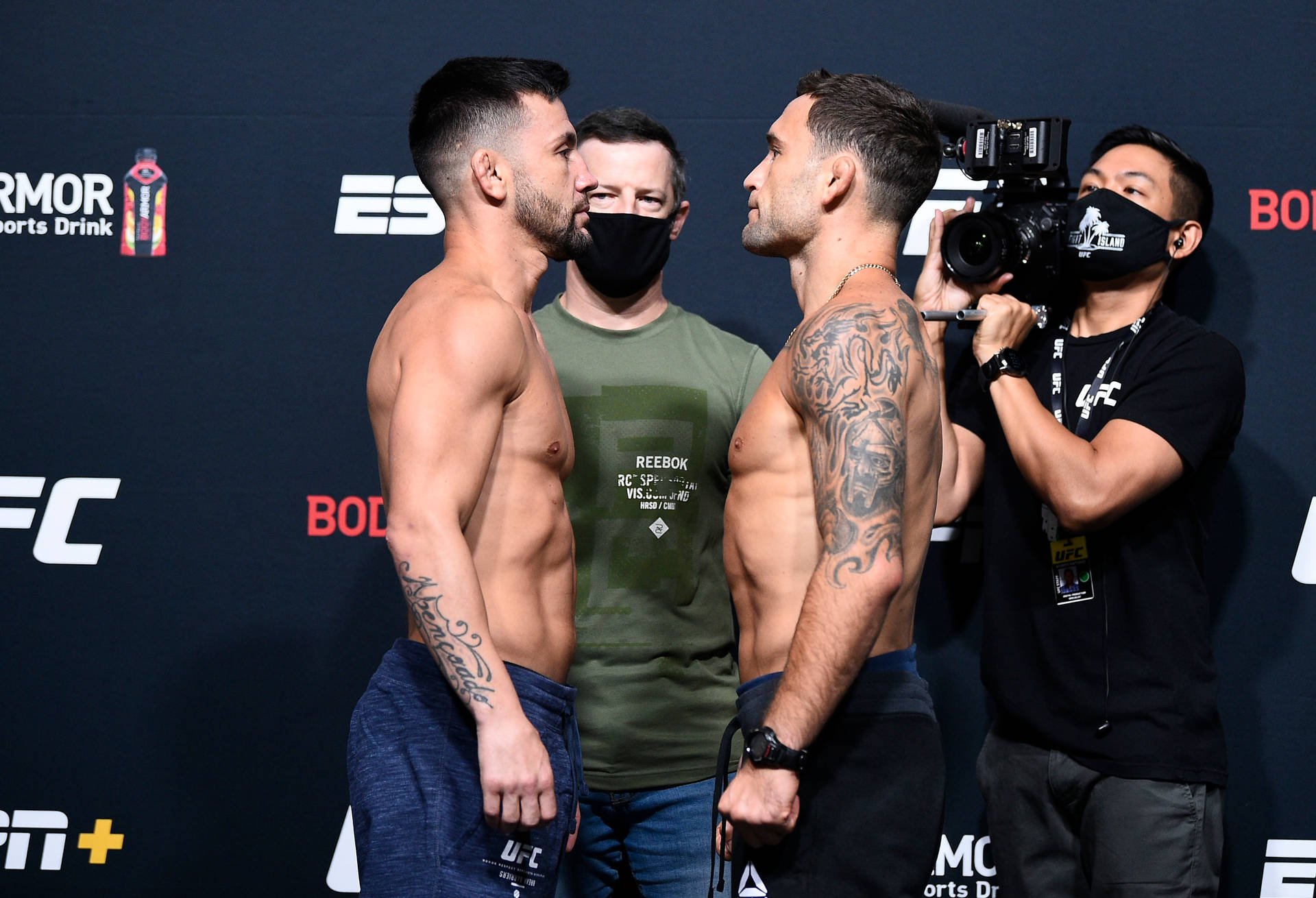 兩名赤裸上身的MMA拳手在UFC稱重儀式上互相凝視，周圍有相機。