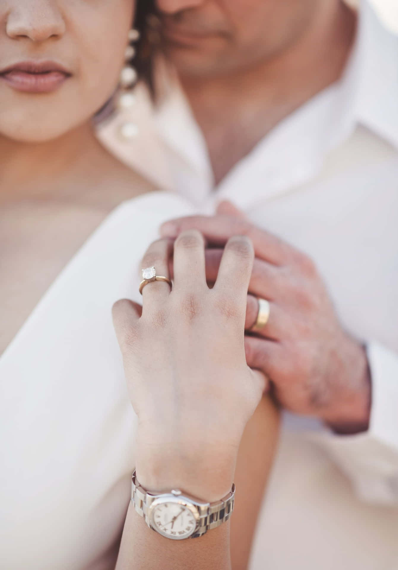 一對情侶的手緊握在一起，展示結婚戒指和手錶。