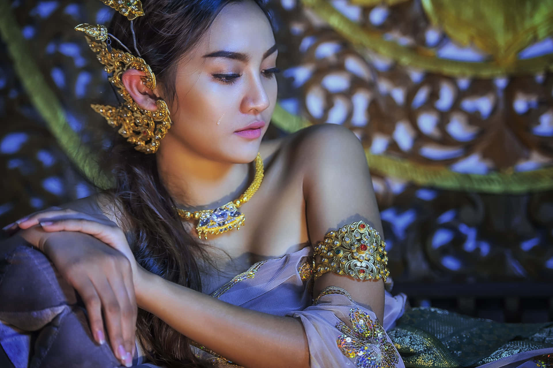 一位佩戴金色泰式珠寶和薰衣草服飾的女性，姿態寧靜。