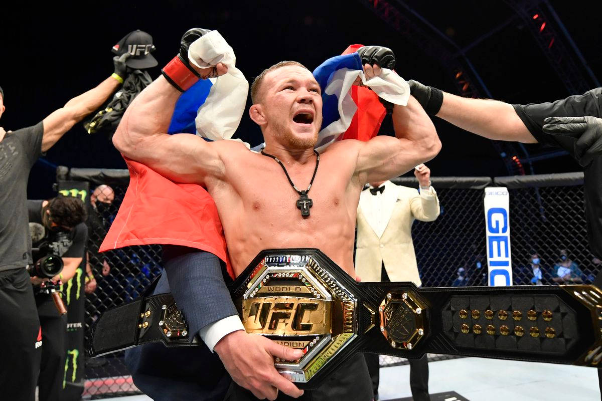 UFC拳手在八角籠中手持冠軍腰帶和旗幟慶祝勝利。