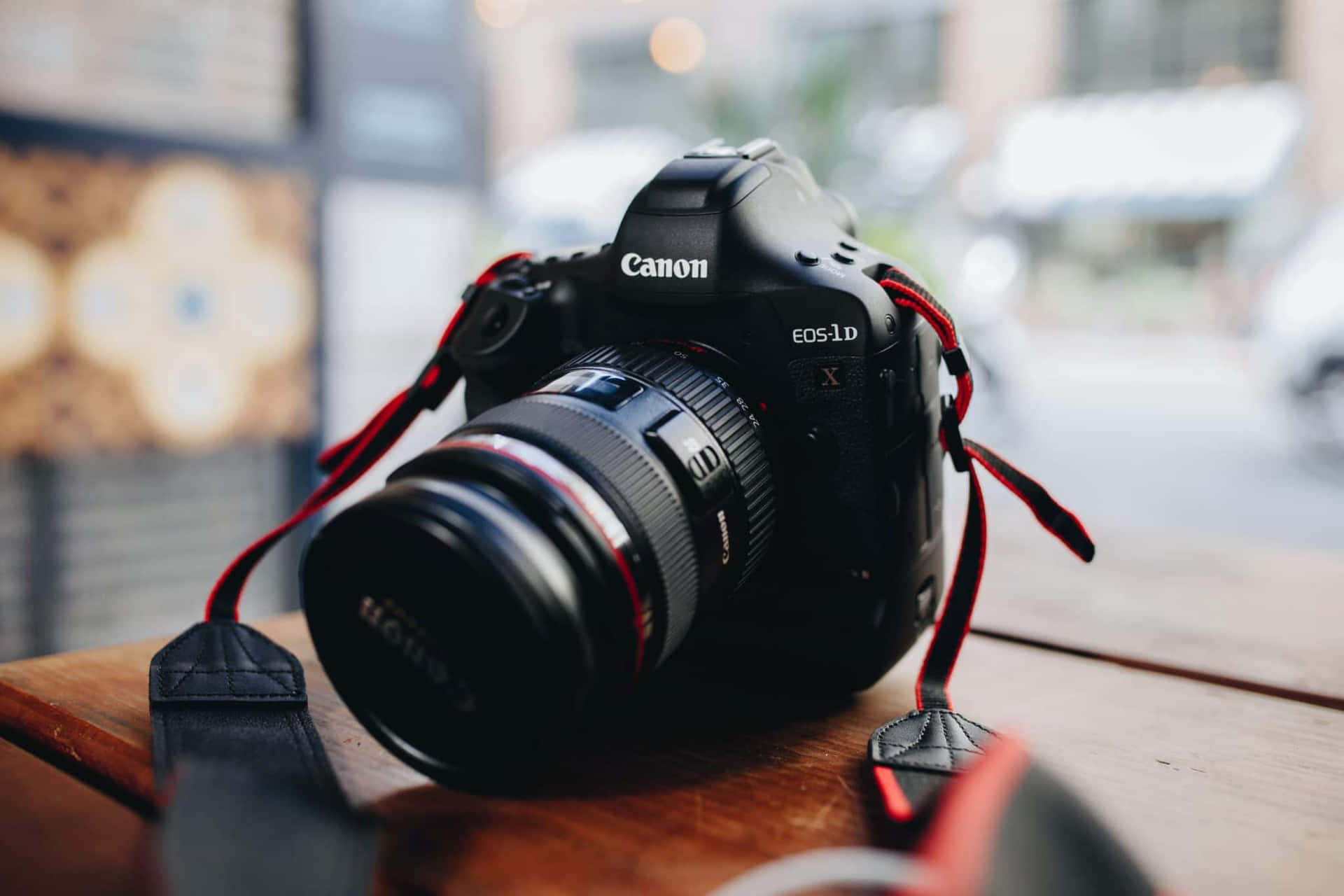 黑色Canon DSLR相機配紅色相機帶，放在城市環境中的木桌上。