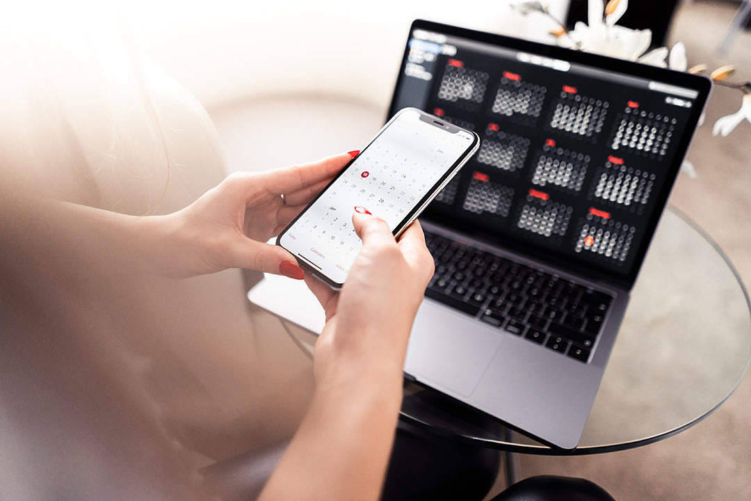使用 MacBook Air 2020 的人 壁紙 — 一個紅指甲的人使用智能手機日曆應用程式，同時手提電腦在玻璃桌上顯示匹配的數碼日曆。