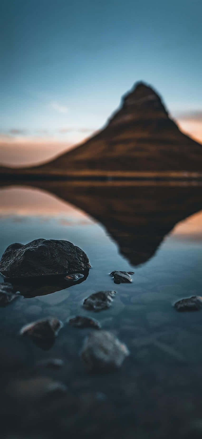 山峰倒映在靜止的水中，前景有岩石，暮色時分。