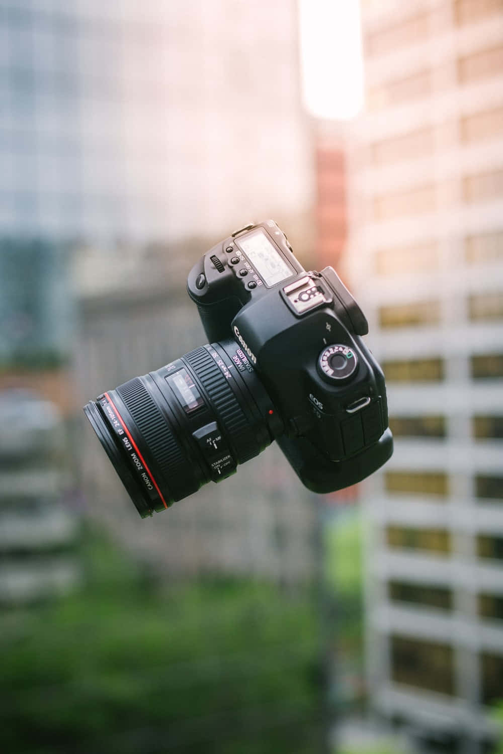 漂浮的 DSLR 相機，背景是模糊的城市和金色光線。 — 相機 壁紙