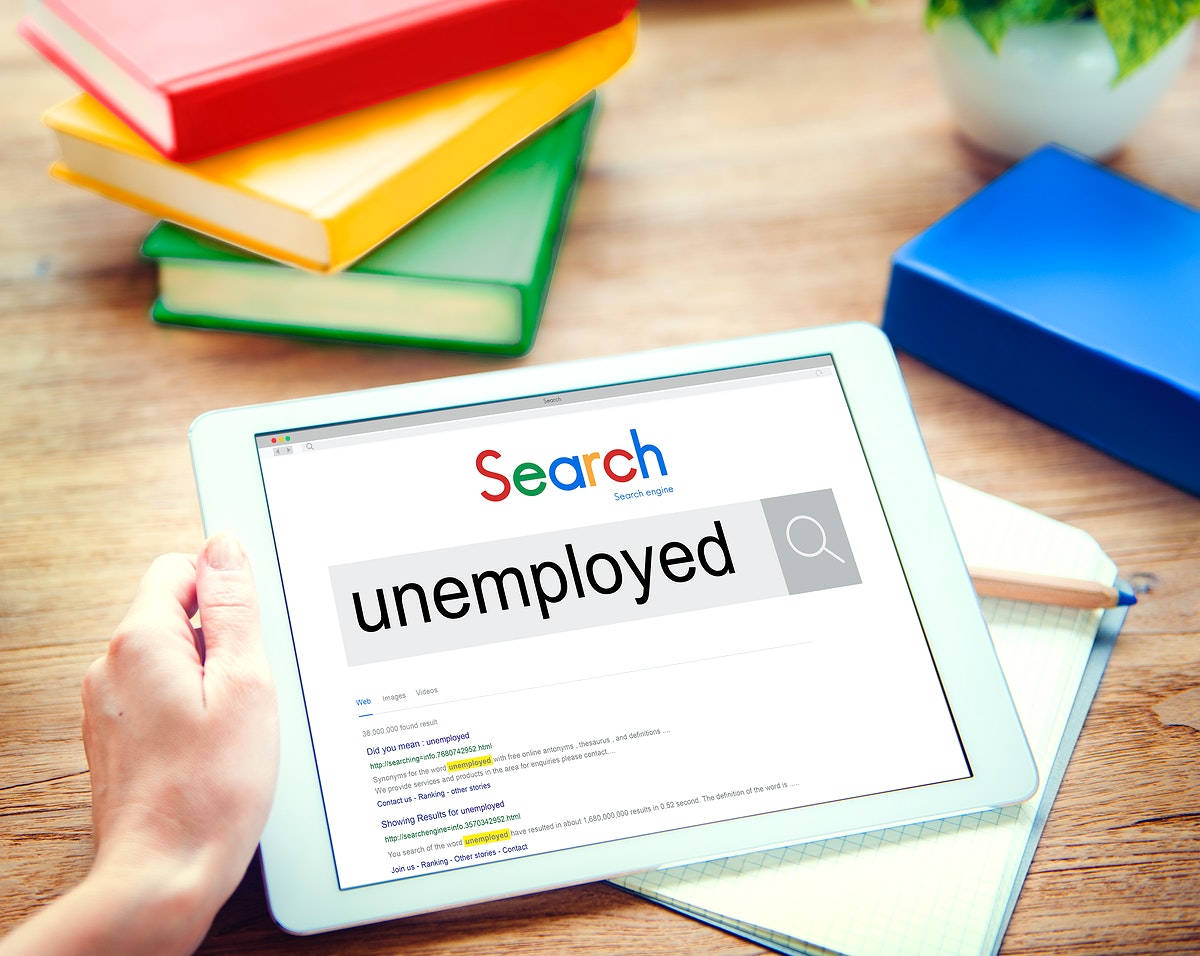 手拿平板電腦搜尋unemployed，與書籍和筆記本在木桌上