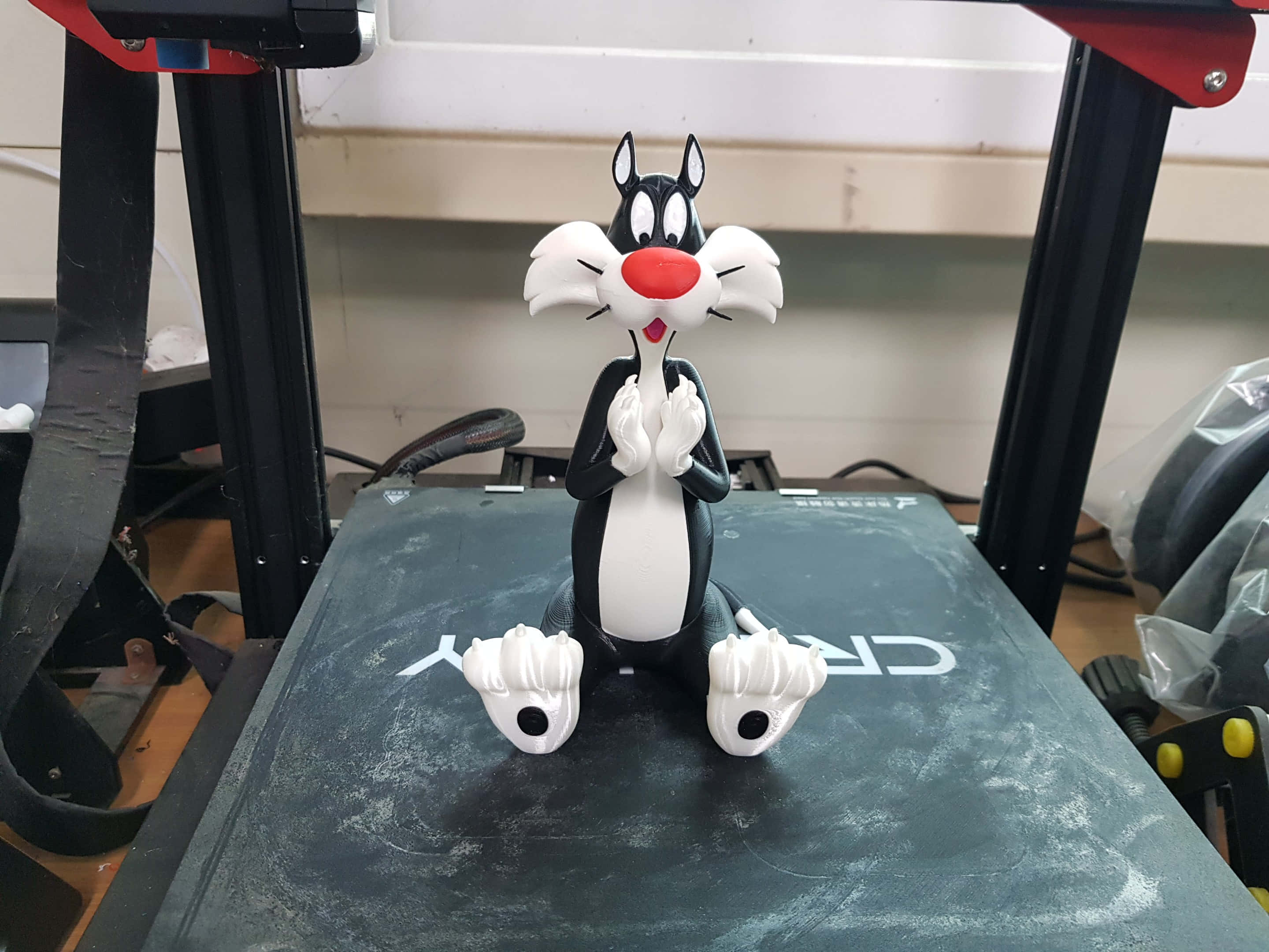 來和 Sylvester The Cat 一起玩吧！ 壁紙 — 一個黑白相間的 Sylvester the Cat 公仔，雙手合攏，雙腳張開，坐在深灰色表面上，周圍是工作室設備。