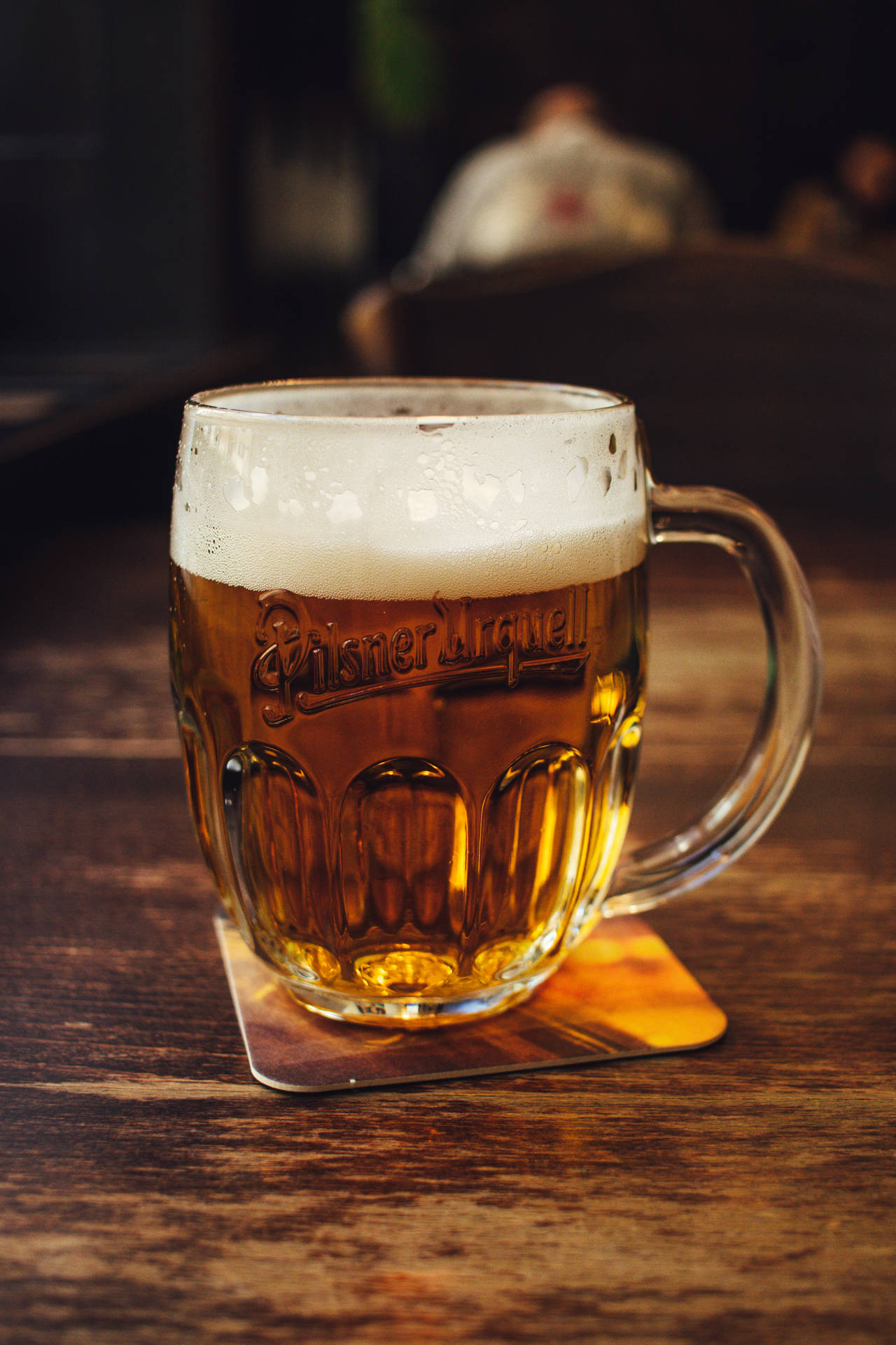 一個冰凍的 Pilsner Urquell 啤酒杯放在木製酒吧枱的杯墊上。