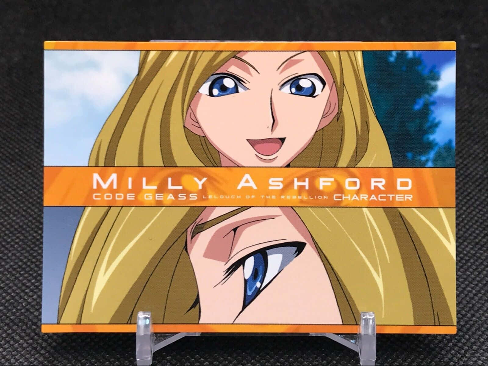 Milly Ashford 桌布 壁紙 — 來自《Code Geass》的動漫角色米莉·阿什福德展示在帶有橙色橫幅和藍色眼睛的收藏卡上。
