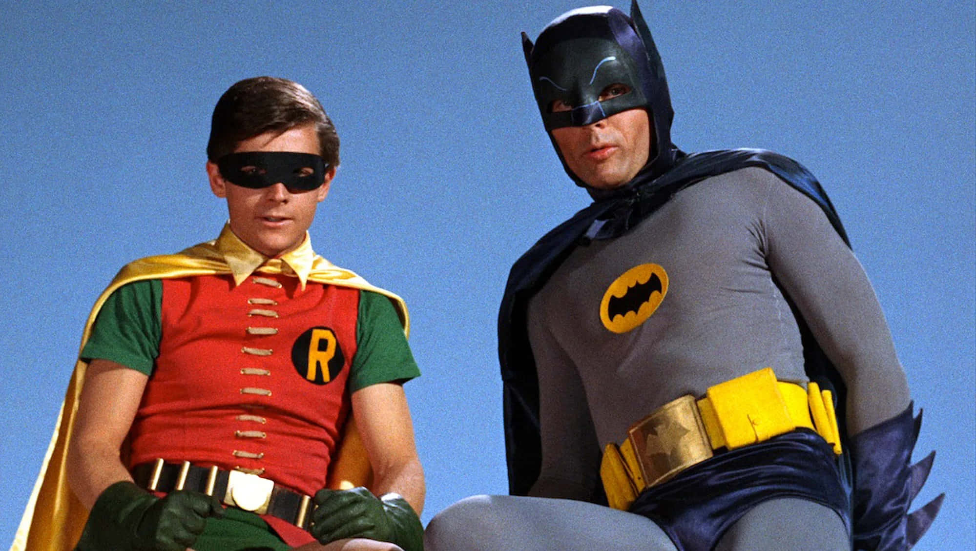 Batman Vs Robin 桌布 壁紙 — 來自1960年代電視節目的蝙蝠俠和羅賓，穿著標誌性的色彩繽紛服裝，在晴朗的藍天下擺姿勢。