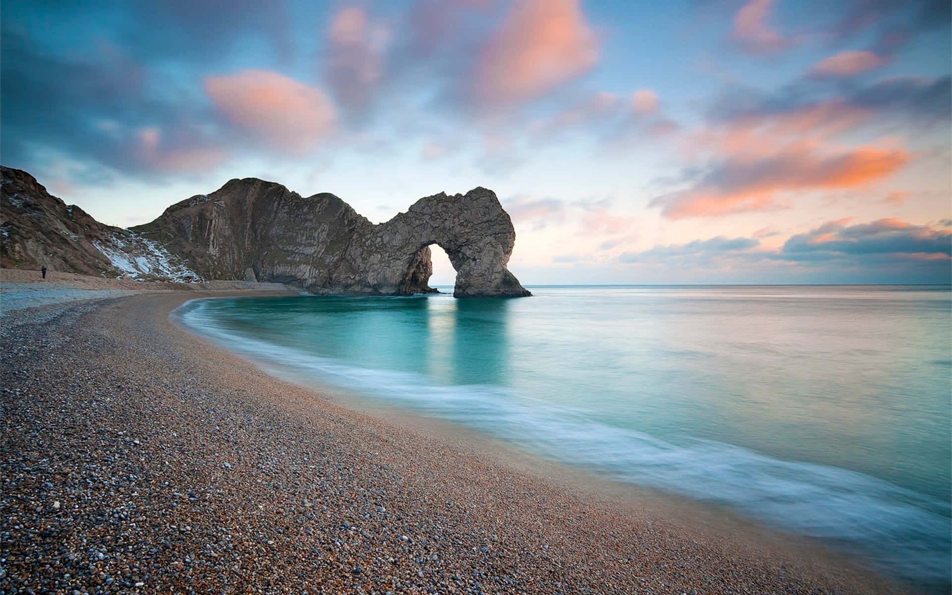日落時分的 Durdle Door 拱門，平靜的藍綠色海水和卵石海灘。