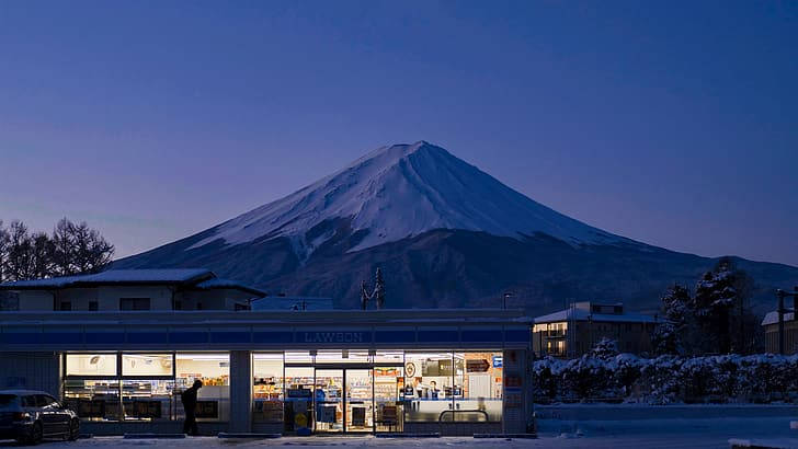 白雪覆蓋嘅富士山喺暮色中聳立喺發光嘅Lawson店後面。