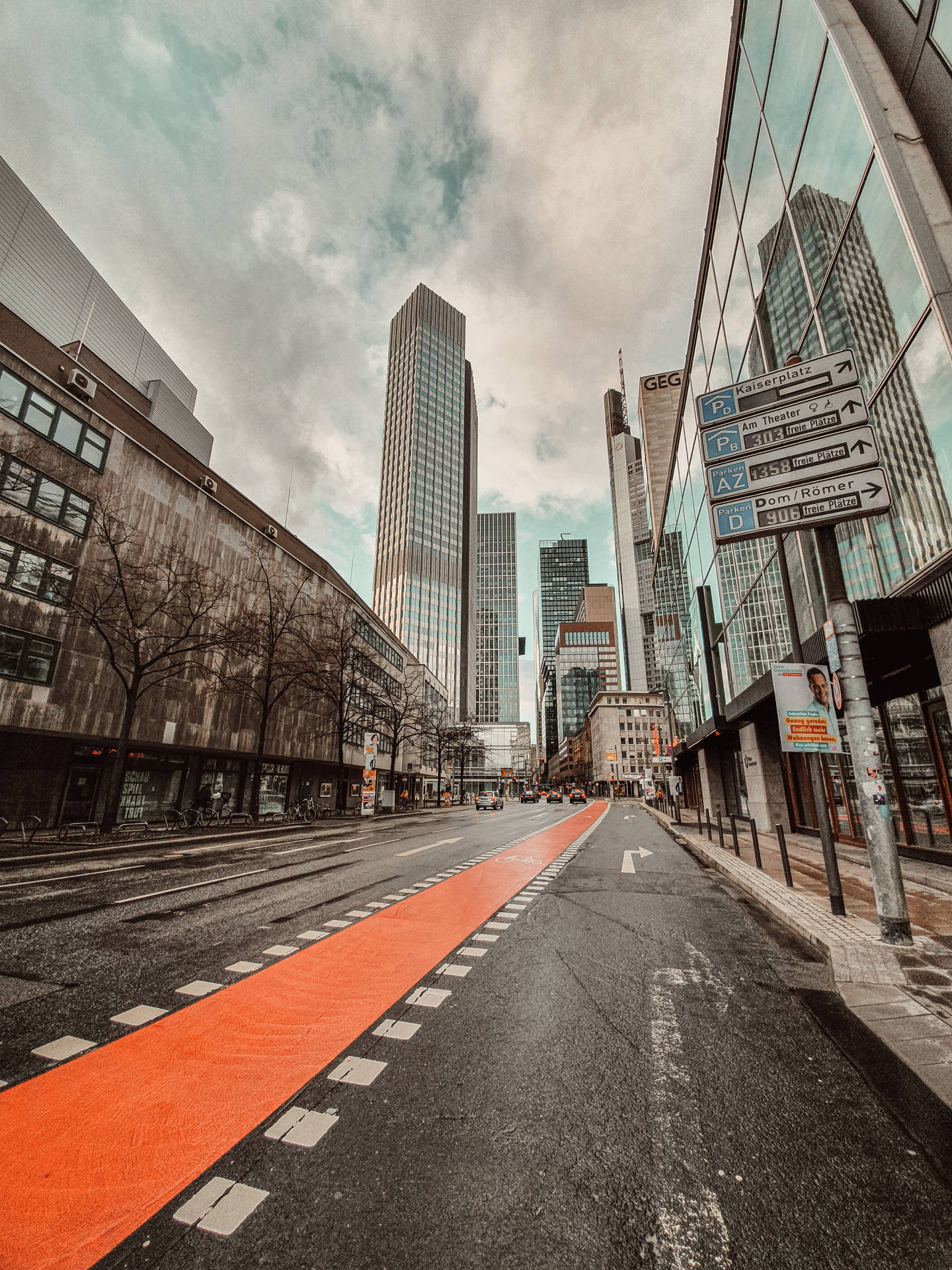 城市街道，有橙色單車道和高大的玻璃建築，天空多雲。
