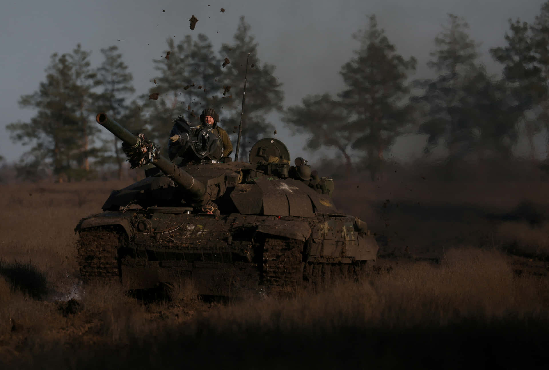 一輛軍用坦克在黃昏的田野中揚起塵土，車上載有士兵。