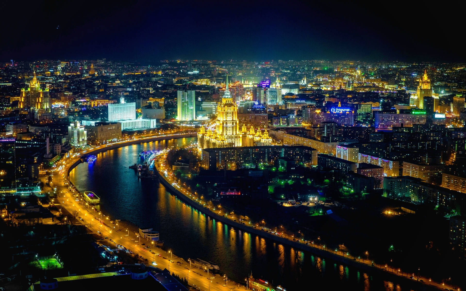俄羅斯夜景空中俯瞰 壁紙 — 充滿活力的城市景觀的夜間鳥瞰圖，發光的河流蜿蜒穿過燈火通明的摩天大樓和橋樑。