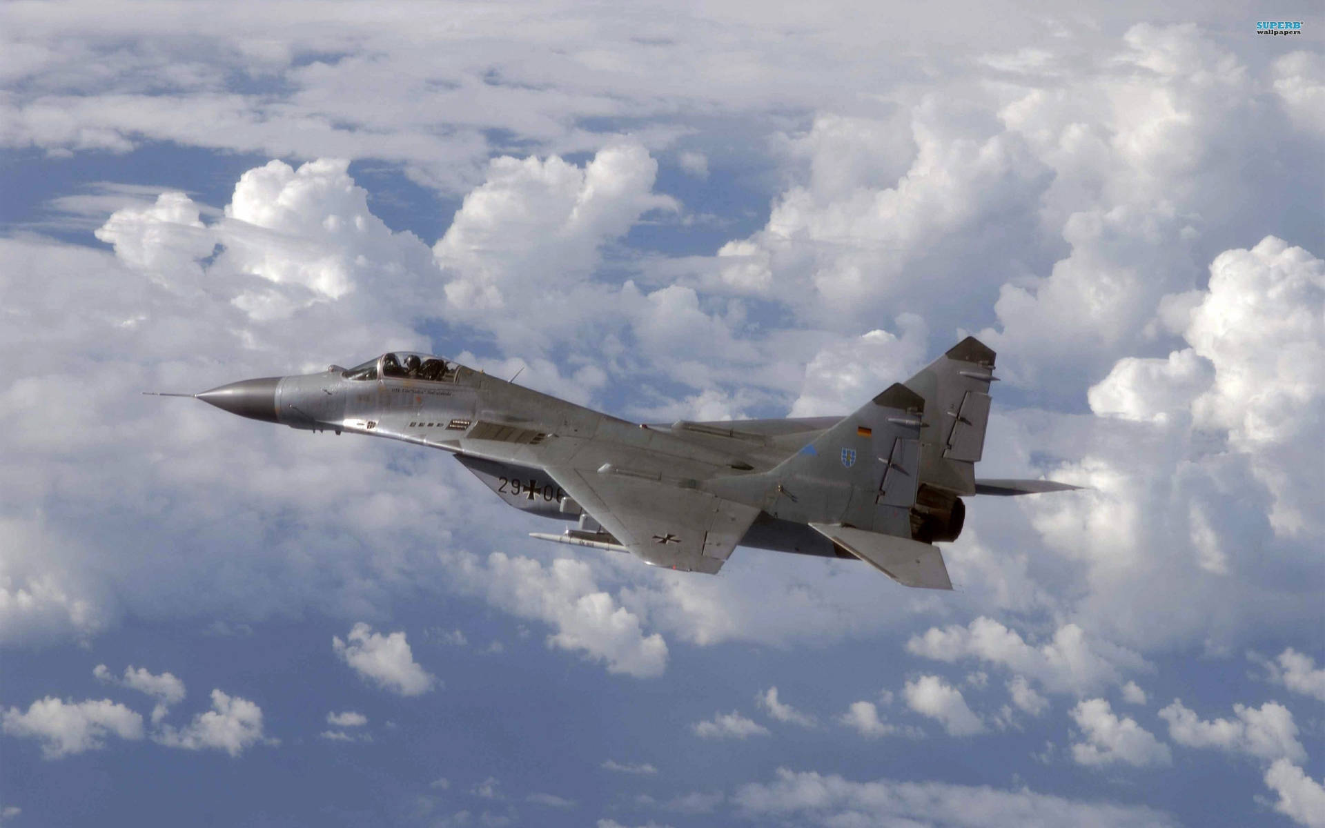 俄羅斯空軍 MiG-29 壁紙 — 一架灰色戰鬥機在點綴著蓬鬆白雲的明亮藍天中翱翔。