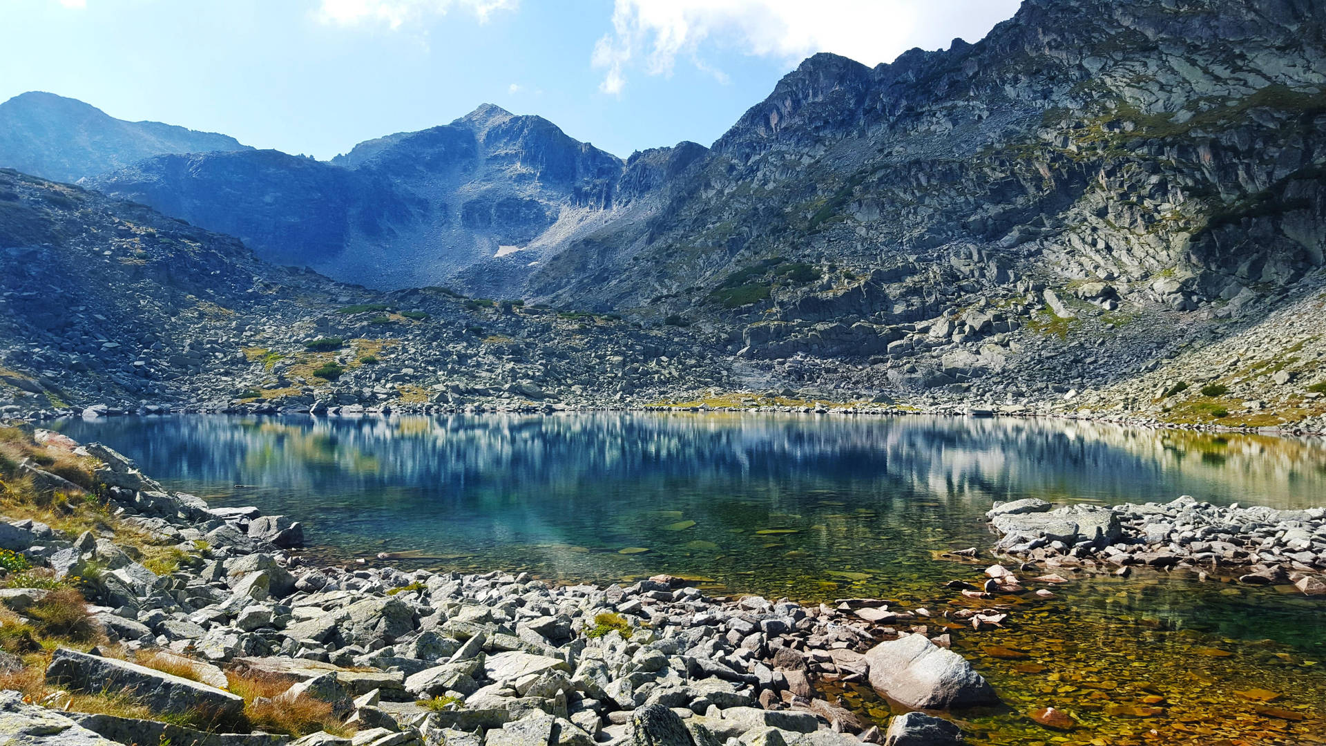 平靜的山湖，四周環繞著岩石地形和巍峨的山峰，天空湛藍。
