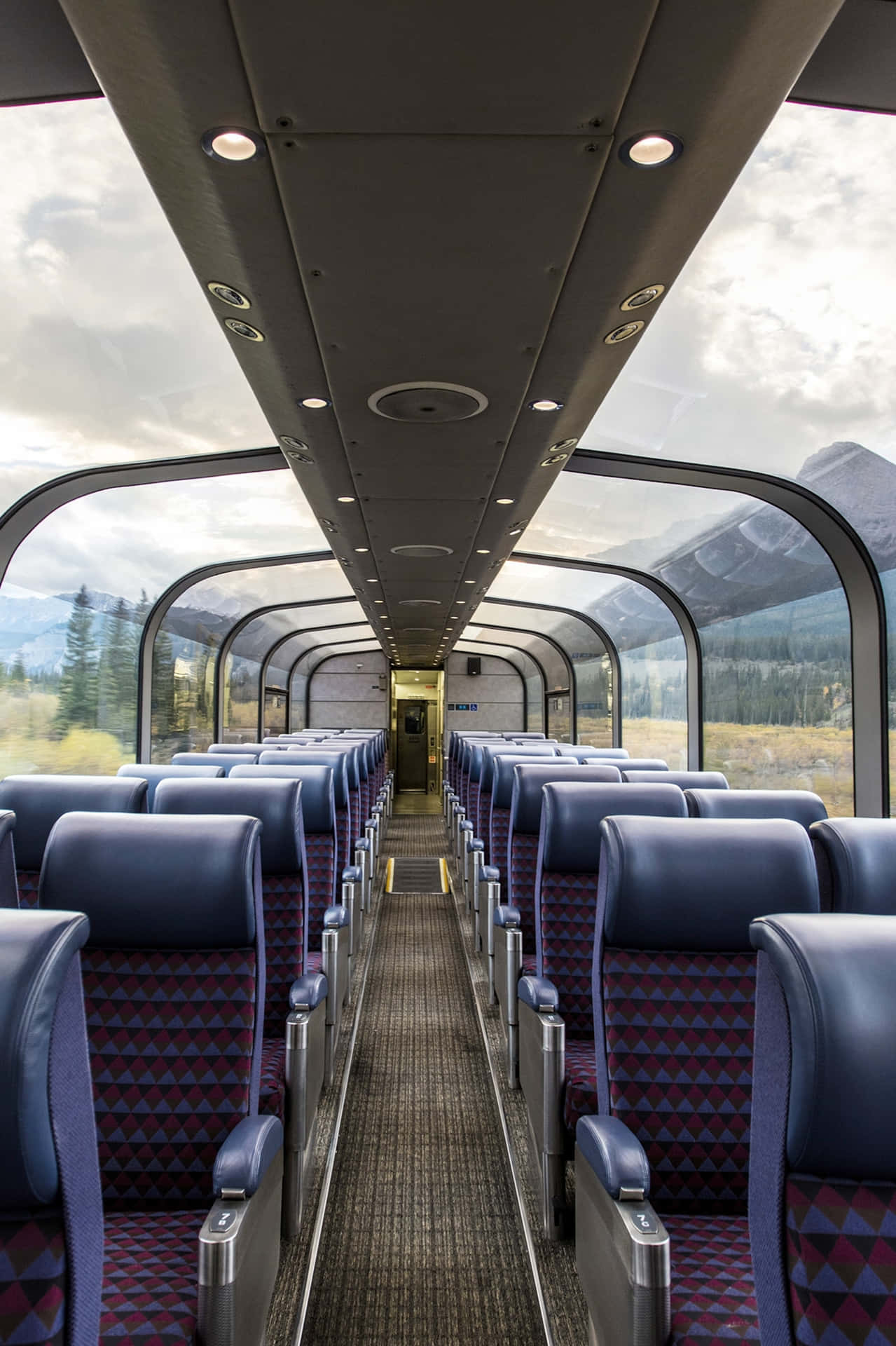 火車車廂，藍色圖案座椅，透過弧形窗戶欣賞山景。